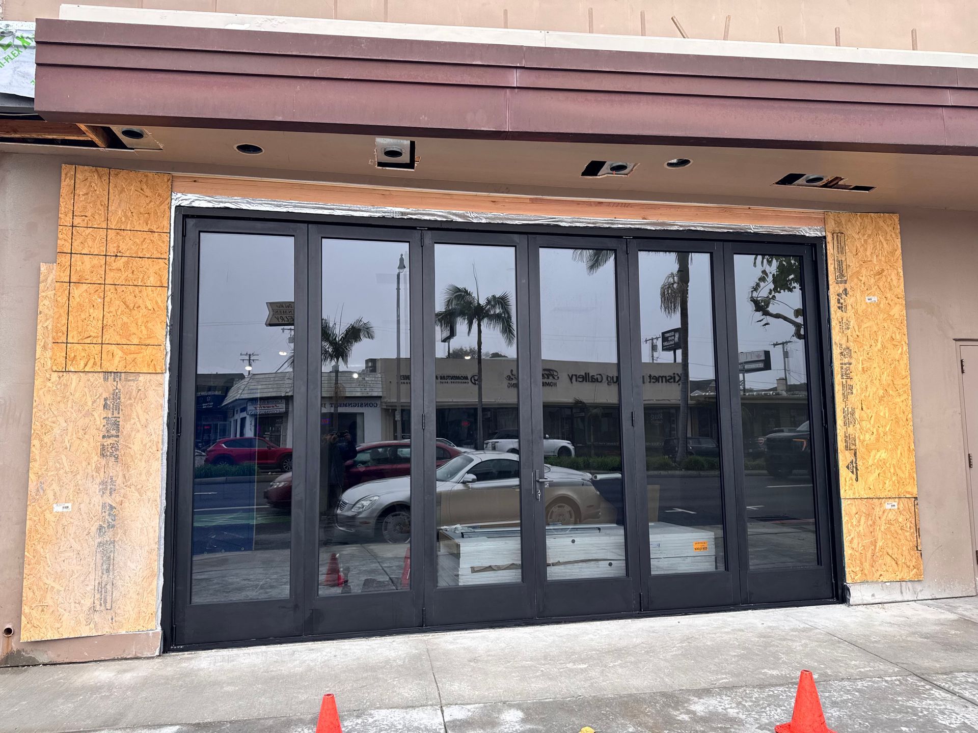 Black folding glass doors on a building under construction, with reflective glass and wooden framing.