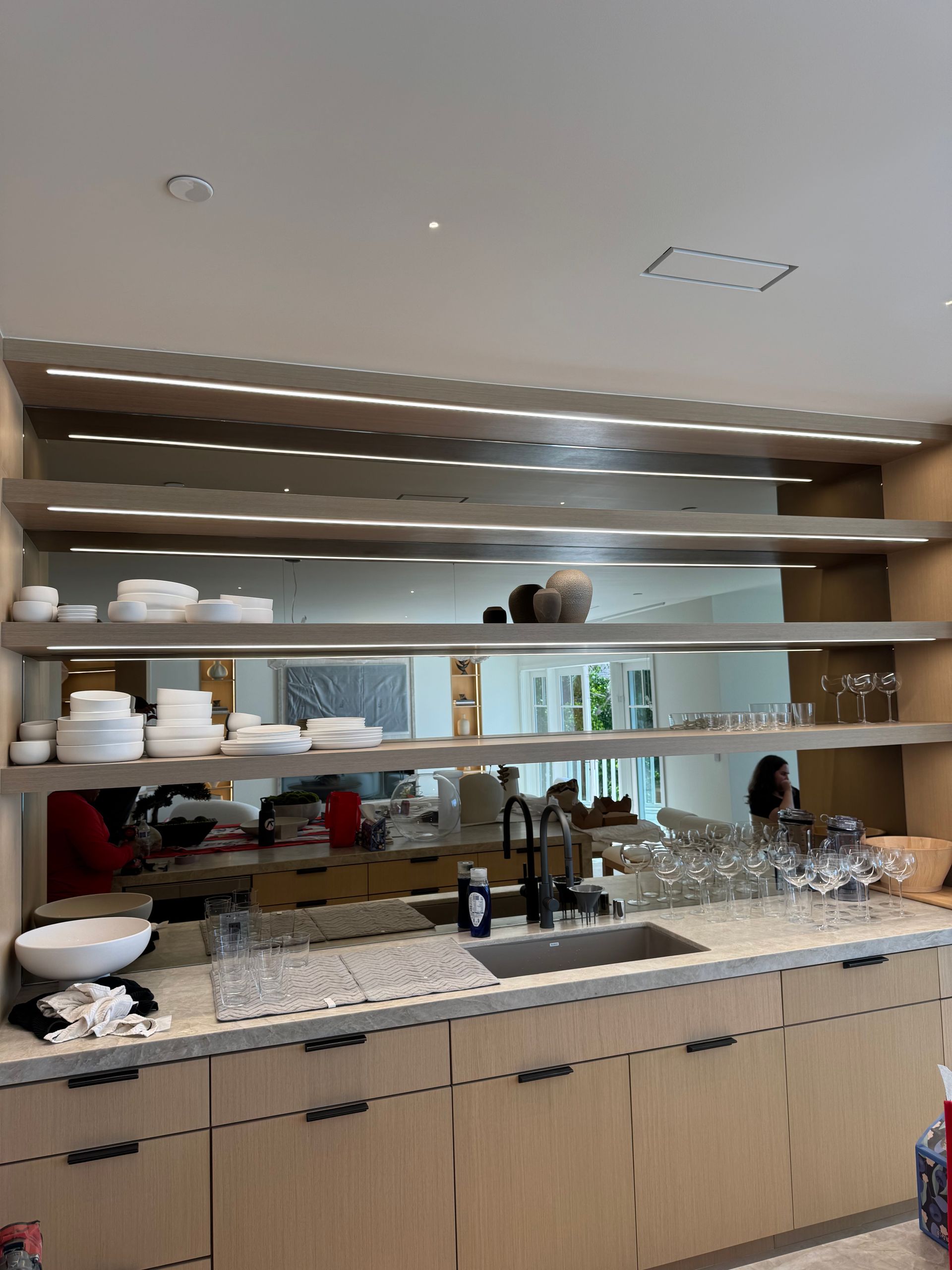Kitchen with light wood cabinets, shelves, and granite countertop, mirrored backsplash, and sink.