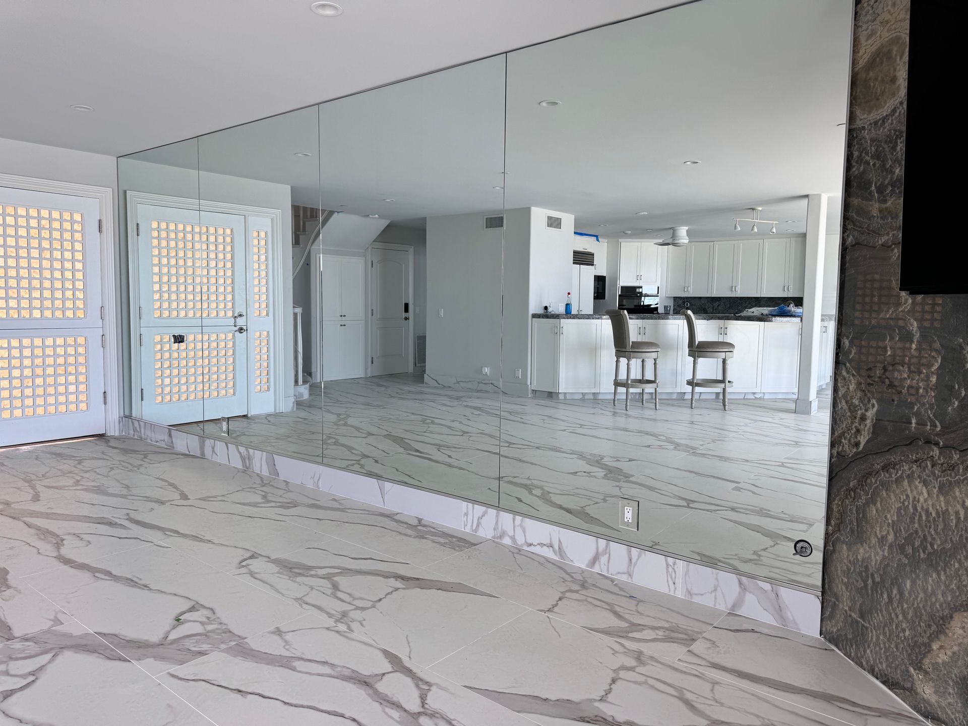 Living room with large mirrored wall, marble flooring, and kitchen in the background.