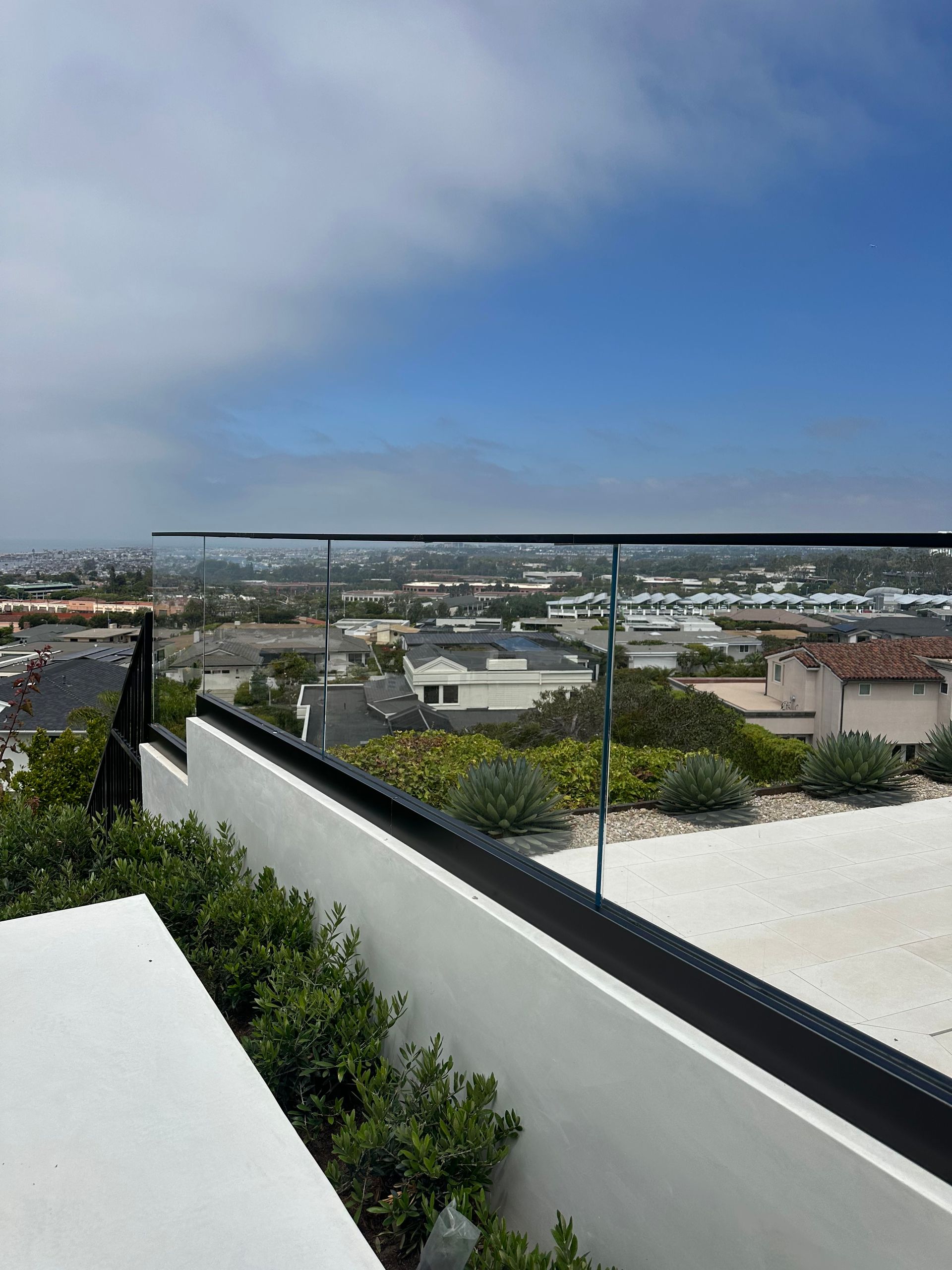 View from a rooftop with a glass railing overlooking a cityscape under a blue sky.
