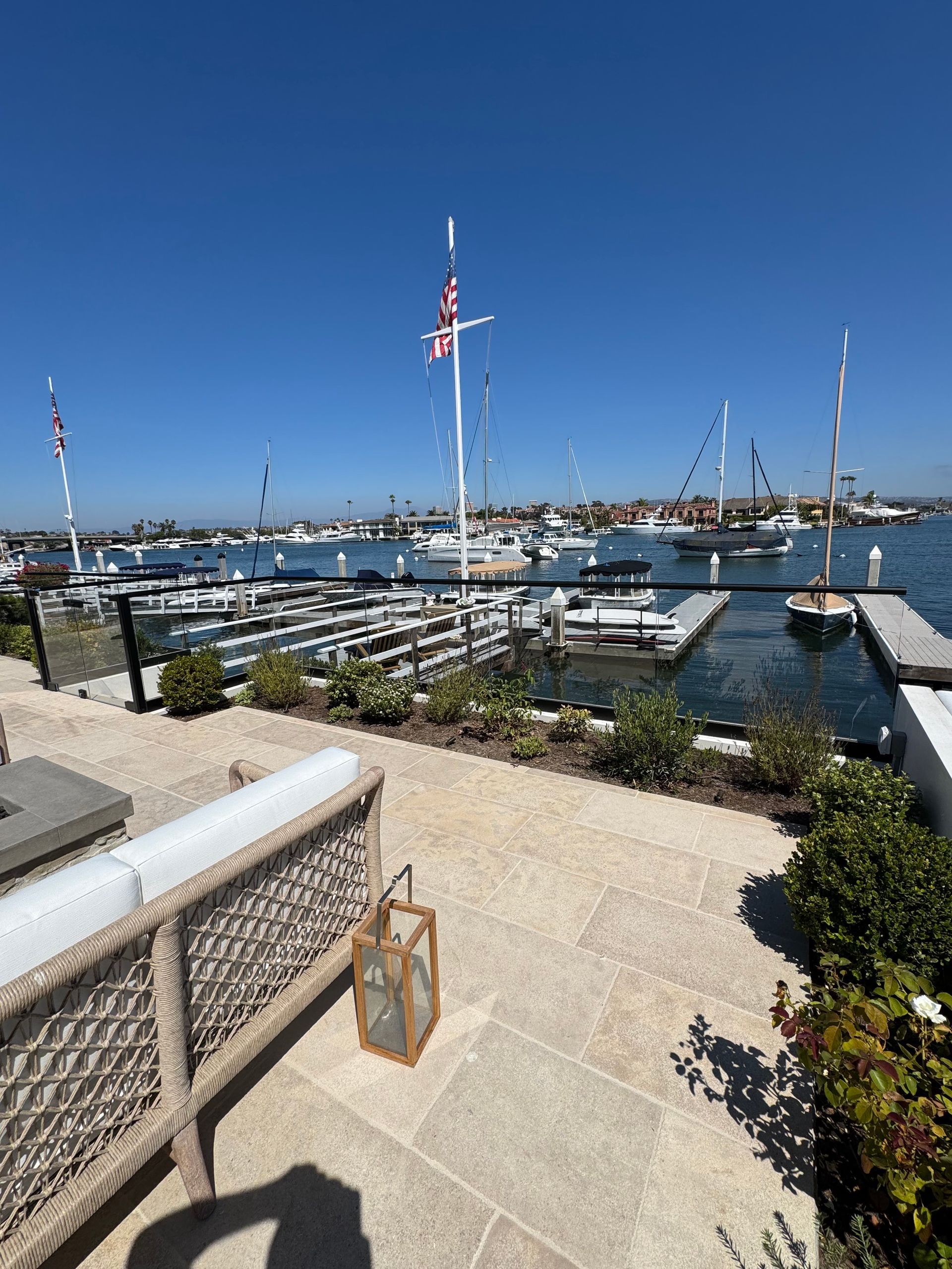 Waterfront patio with marina view, boats, clear blue sky.