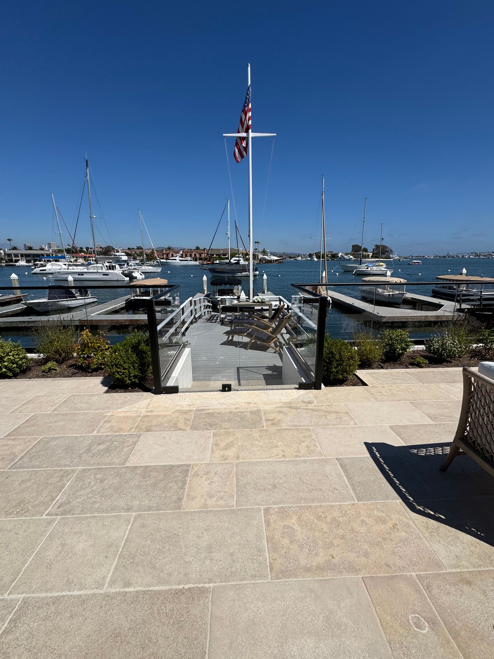 Stone patio overlooking a harbor with a boat dock and boats under a blue sky.