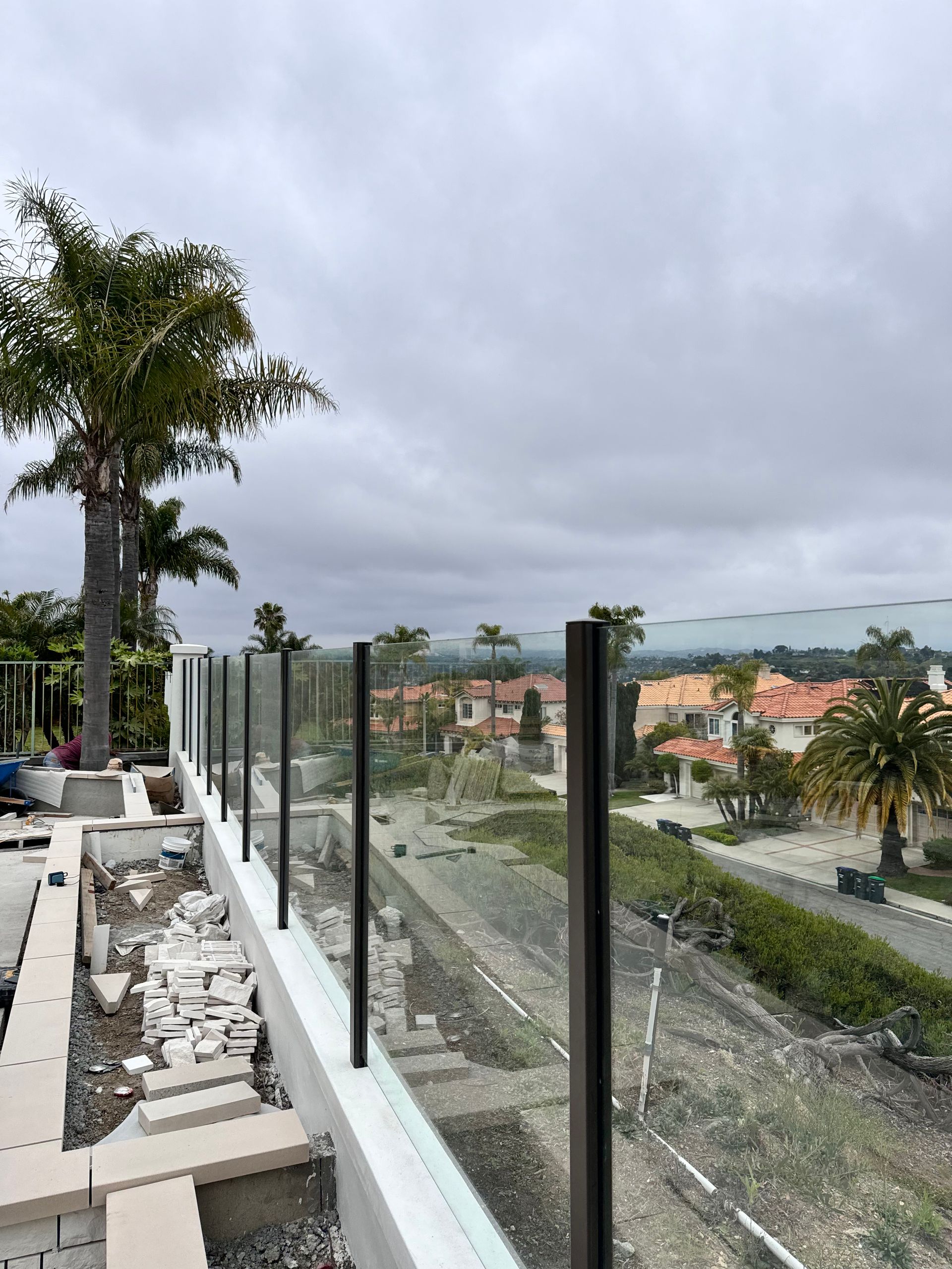 Glass railing on a deck with a view of a neighborhood under an overcast sky.