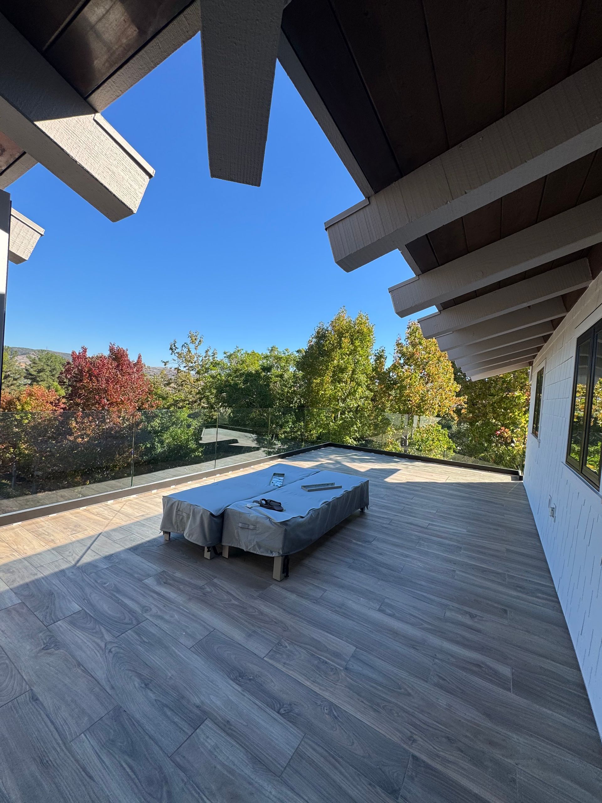 Wooden deck with covered furniture, trees with fall foliage, and a blue sky.