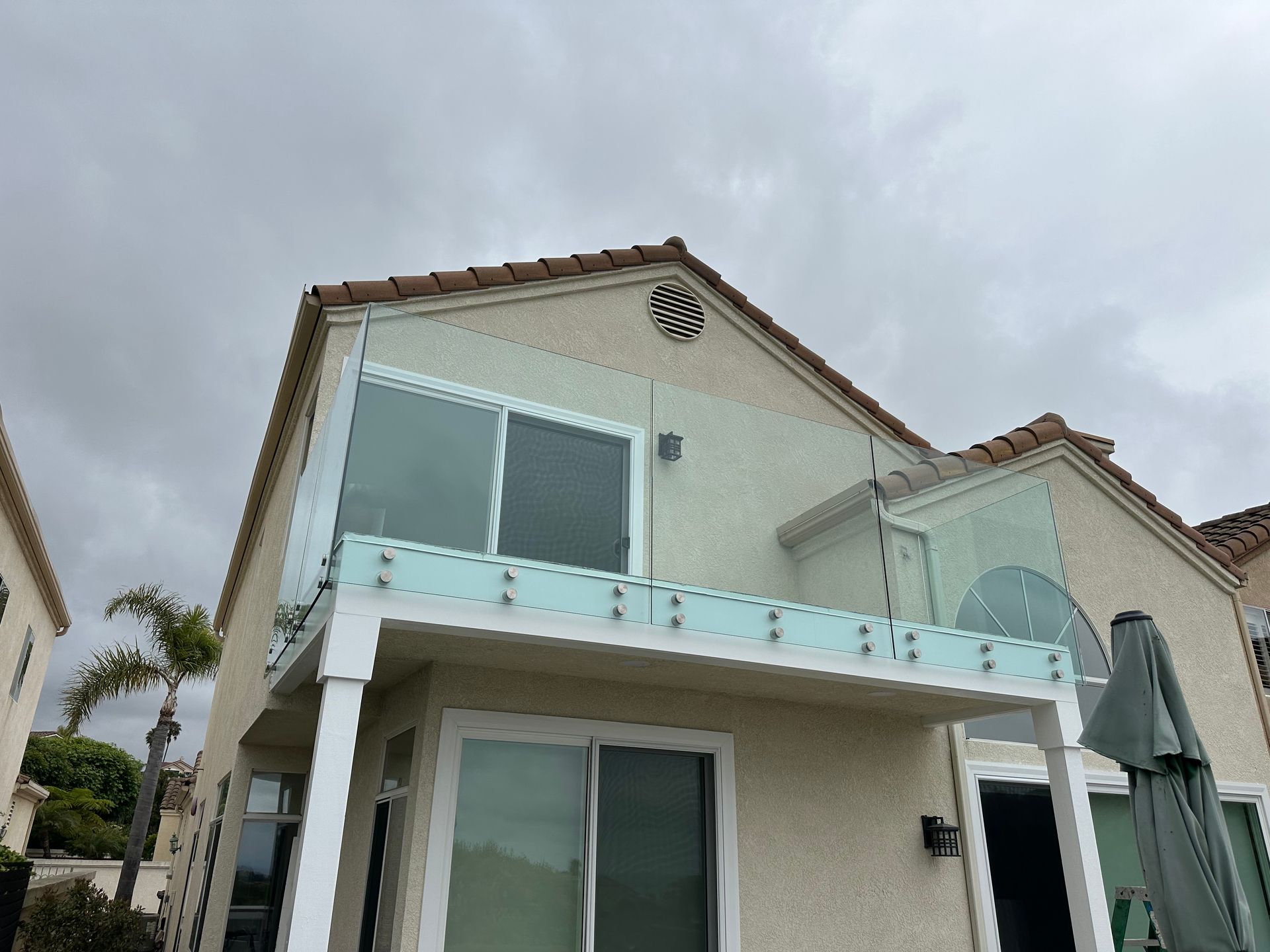 Two-story house with glass balcony railings under an overcast sky.