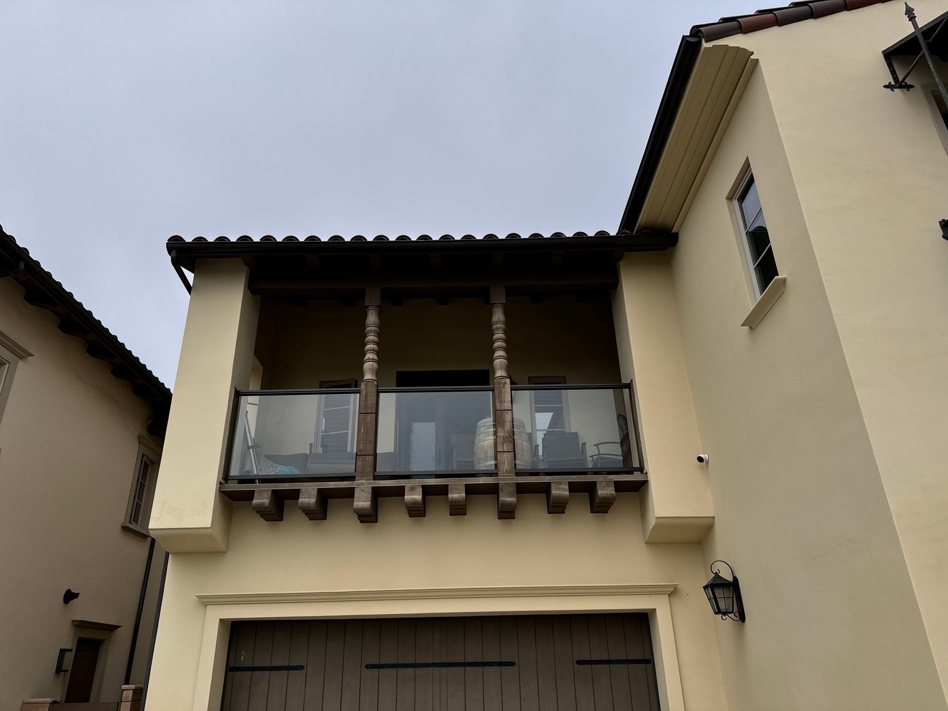 Beige house with a balcony over a garage. The balcony has wooden posts and glass railing.