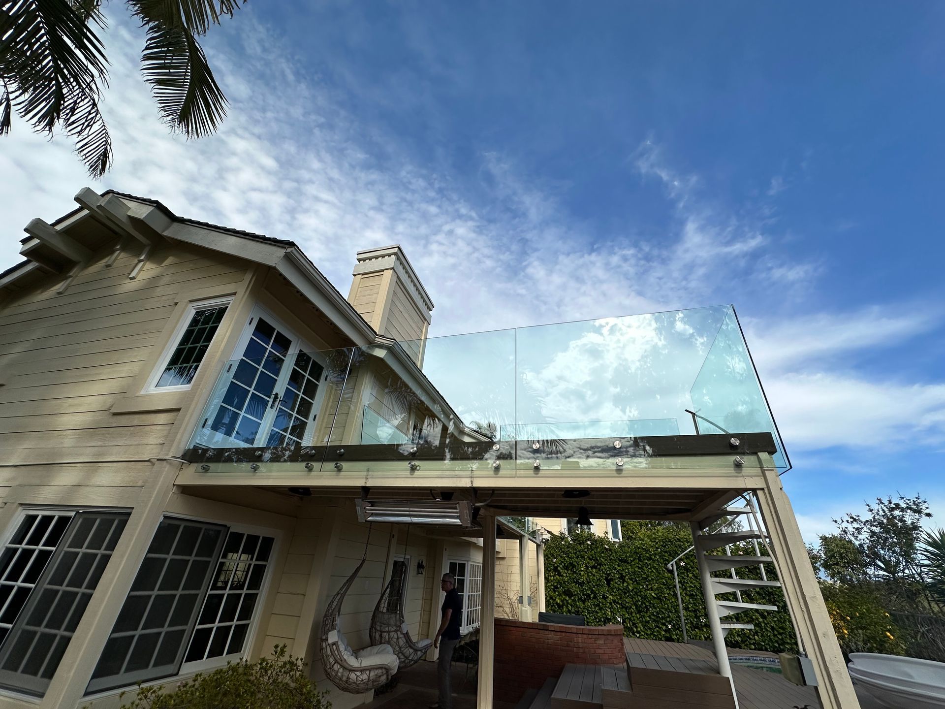 House with glass balcony railing against a blue sky with clouds.