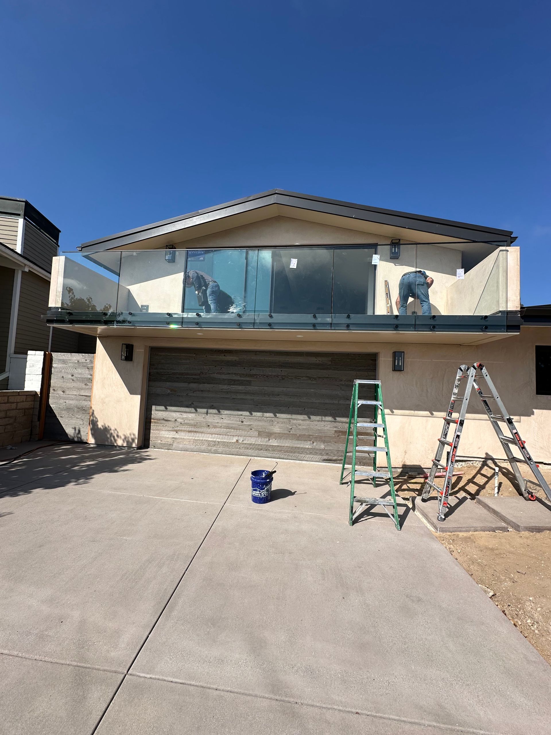 House exterior with upper balcony, closed garage, ladders, and blue sky.