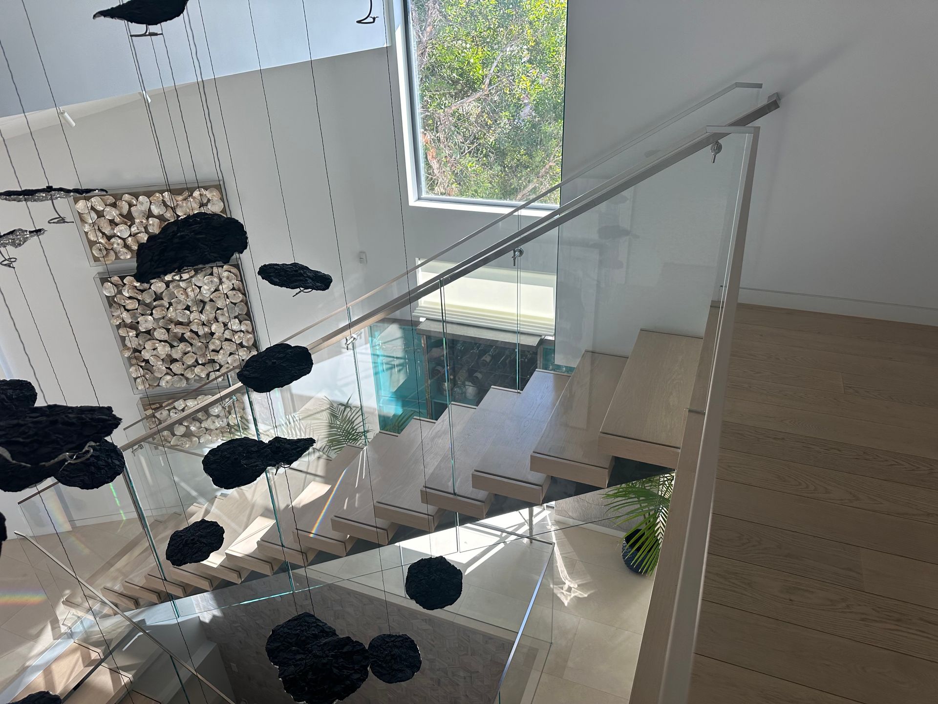 Modern staircase with glass railing and decorative black art installation, wooden steps.