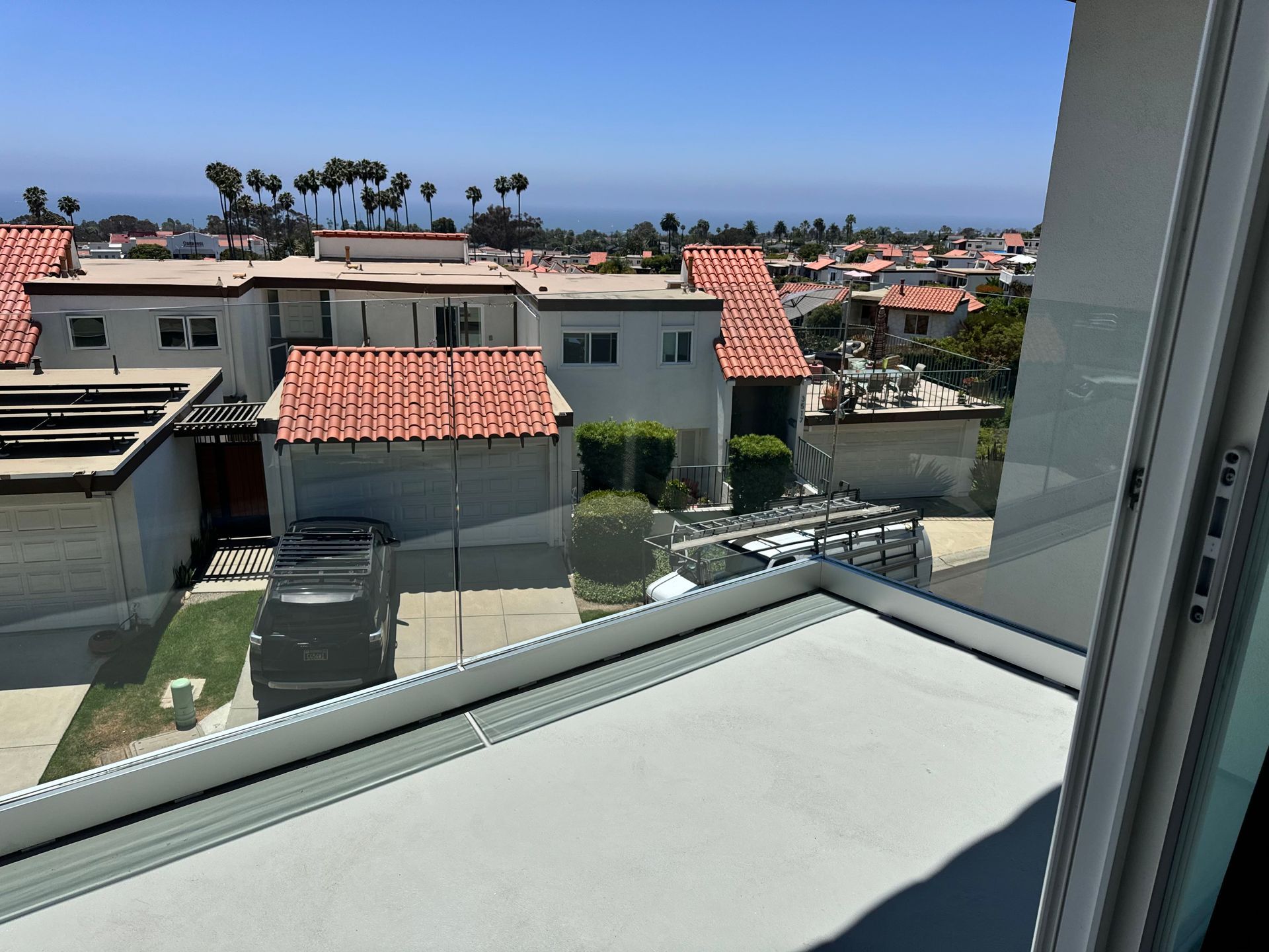 View from a balcony of rooftops, a distant ocean, and a clear blue sky.