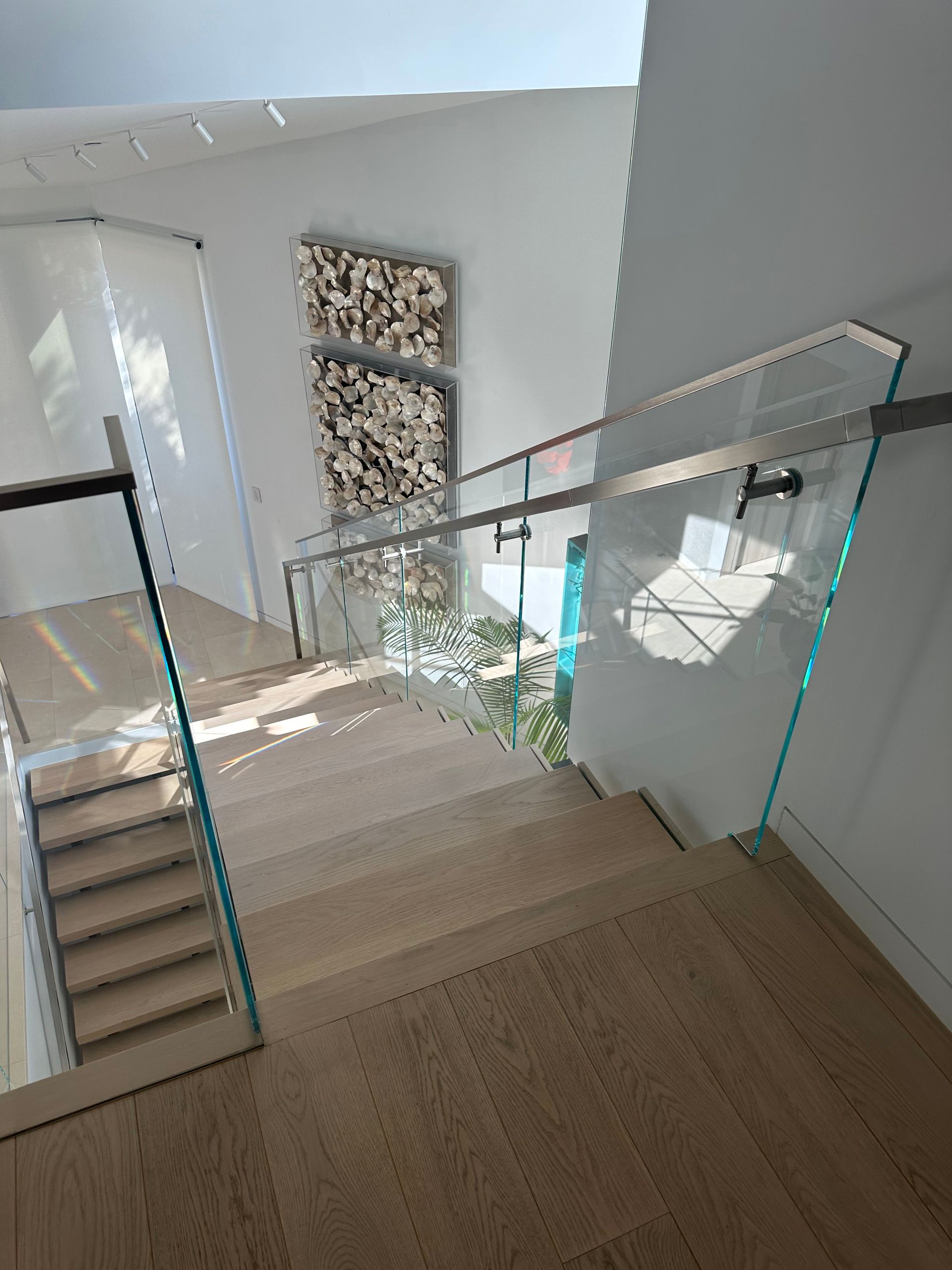 Staircase with glass railing, light wood steps, and artwork on a white wall.