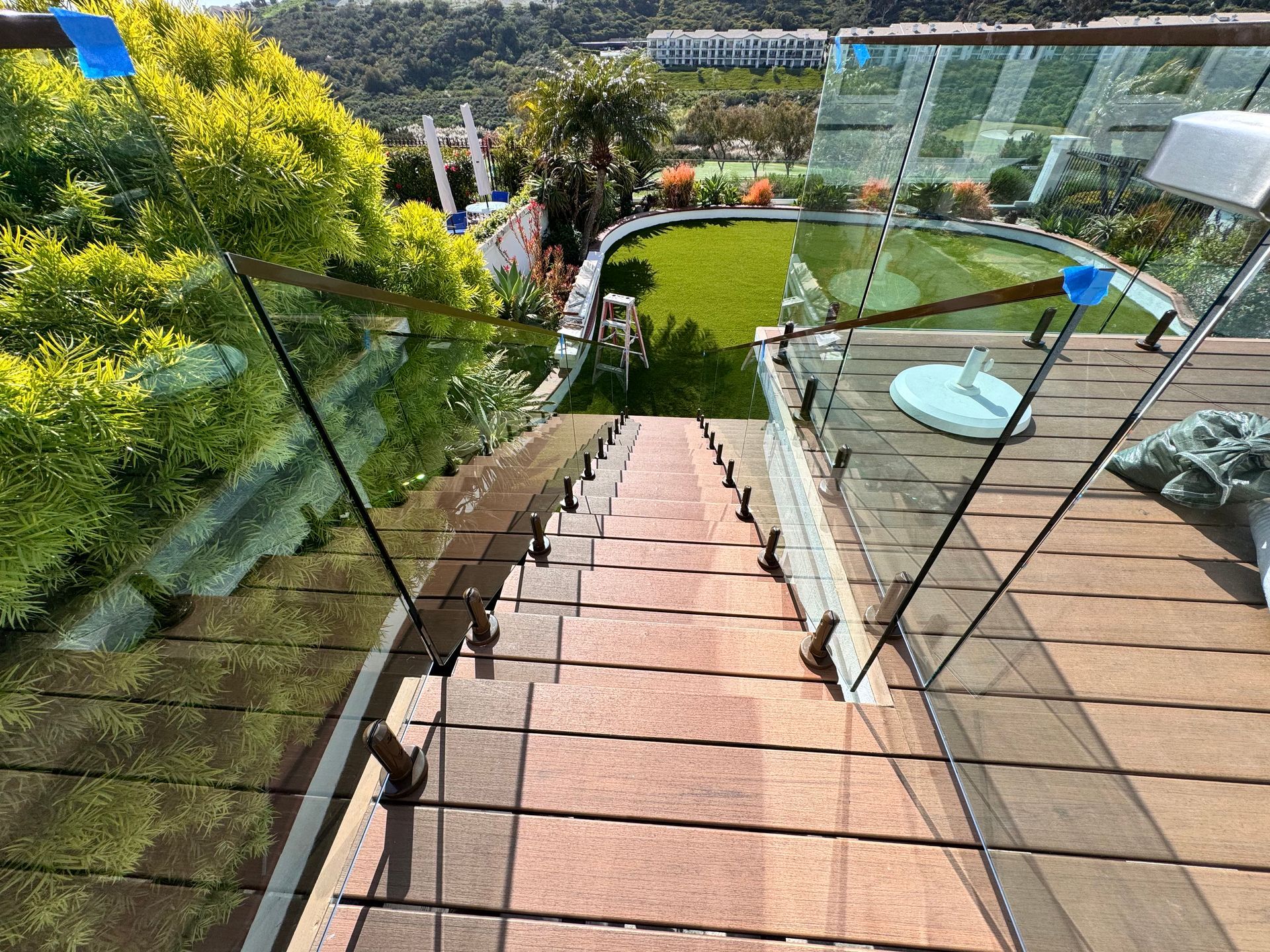 Stairs descend from a rooftop with glass railings towards a putting green in a sunny outdoor setting.