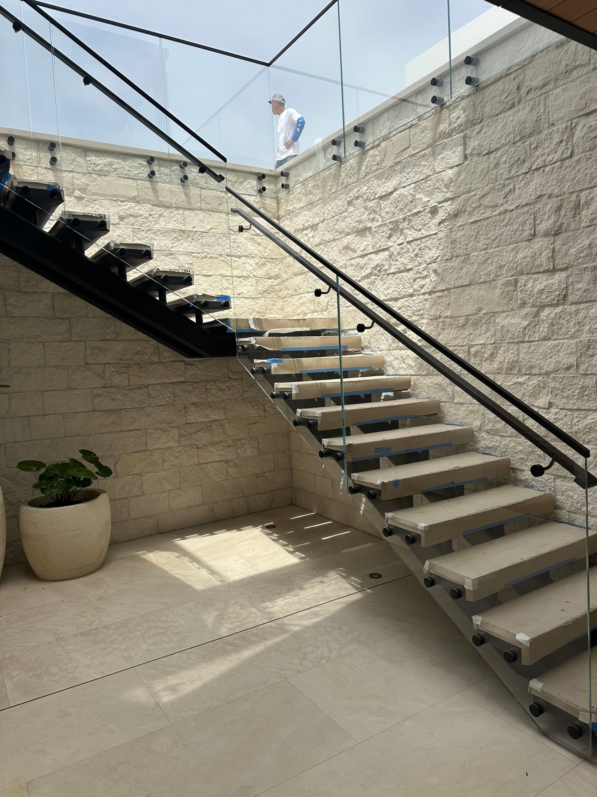 Staircase with glass railing and textured stone wall. A person stands at the top.