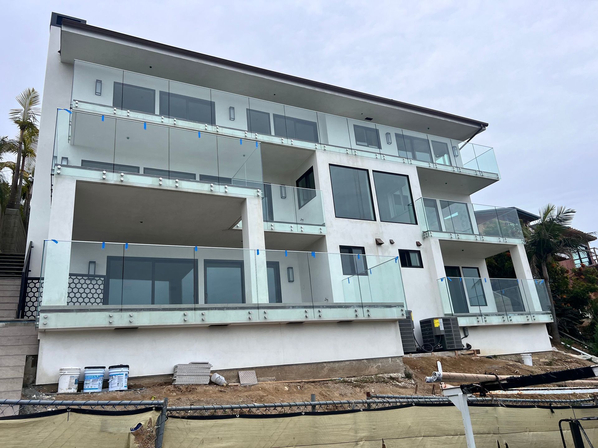 Modern white multi-story house with glass balconies, under construction.