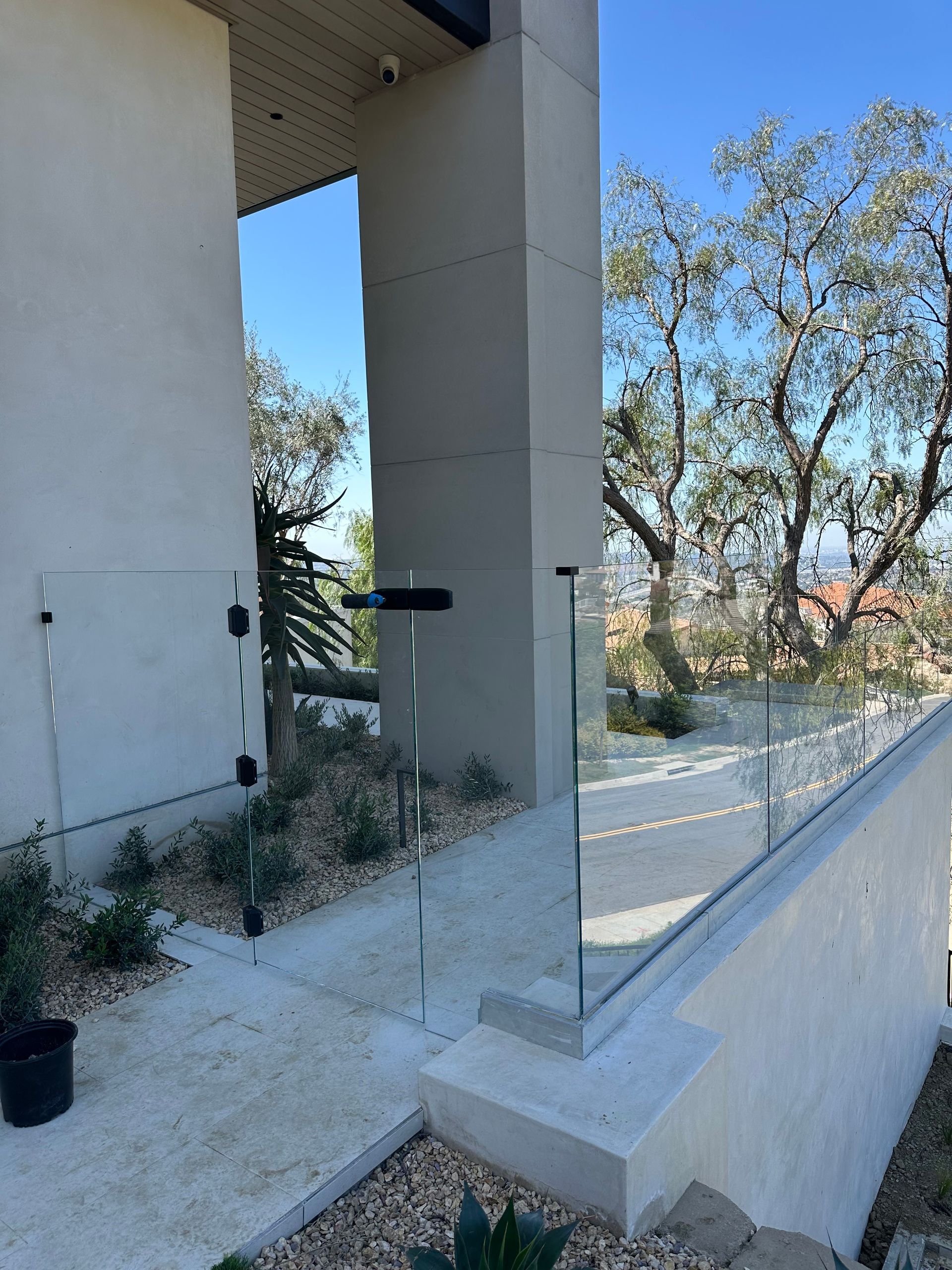Exterior view of a modern house with glass railing, concrete path, and small garden, against a blue sky.