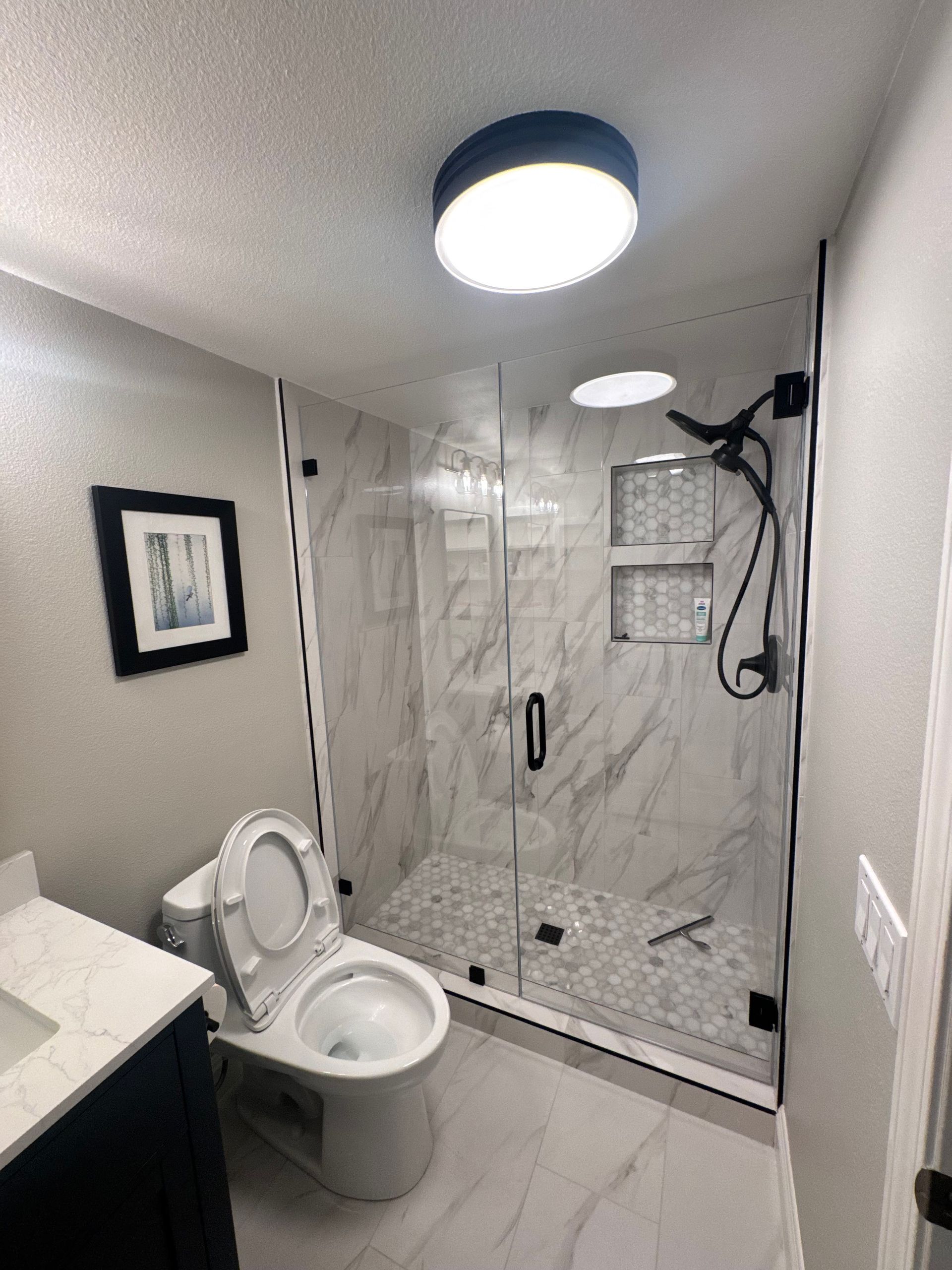 Modern bathroom with marble shower, glass door, toilet, vanity, and overhead lighting.