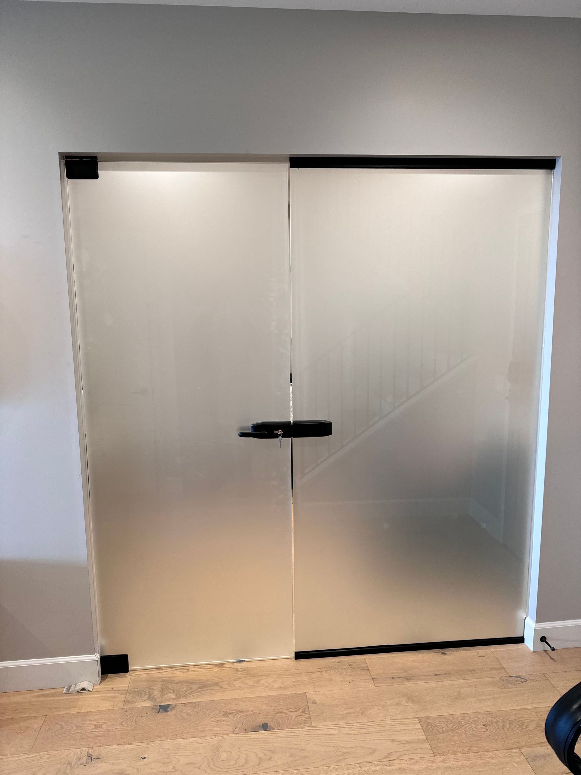 Frosted glass double doors with black hardware, set in a light-colored wall.