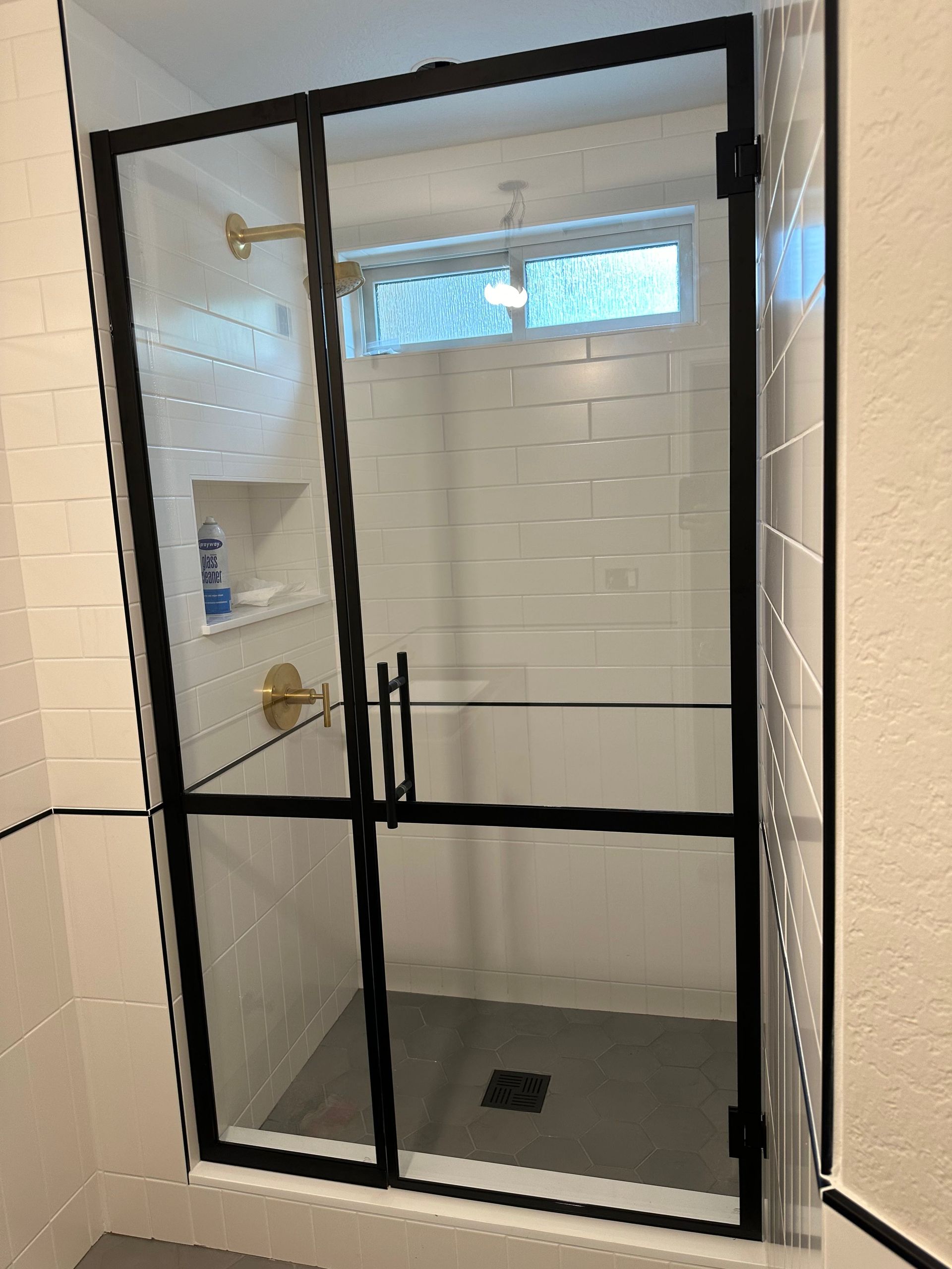 Black framed glass shower enclosure in a bathroom with white tile walls and gold fixtures.