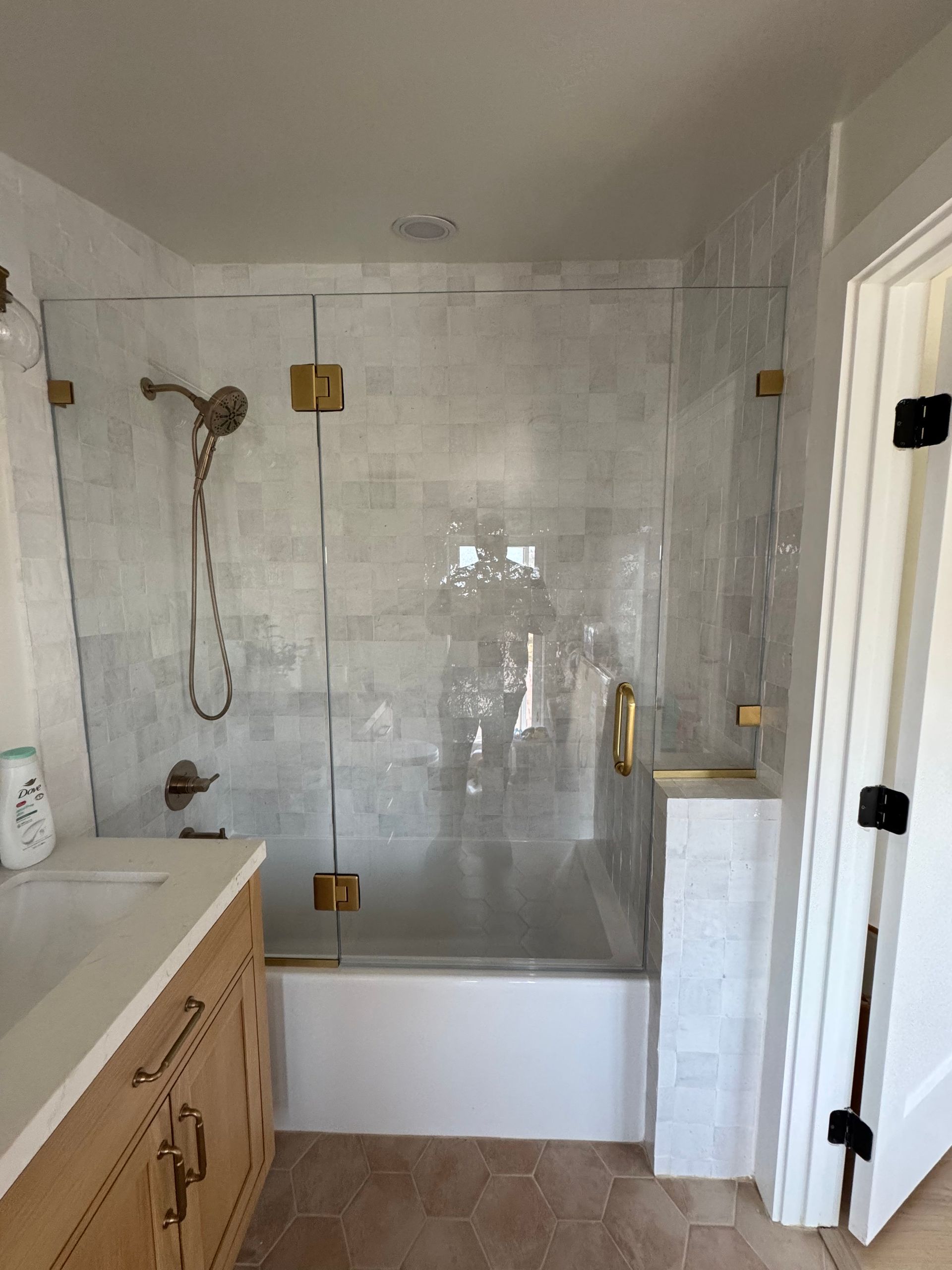 Bathroom with a glass shower door and gold hardware, white tile, and wooden vanity.