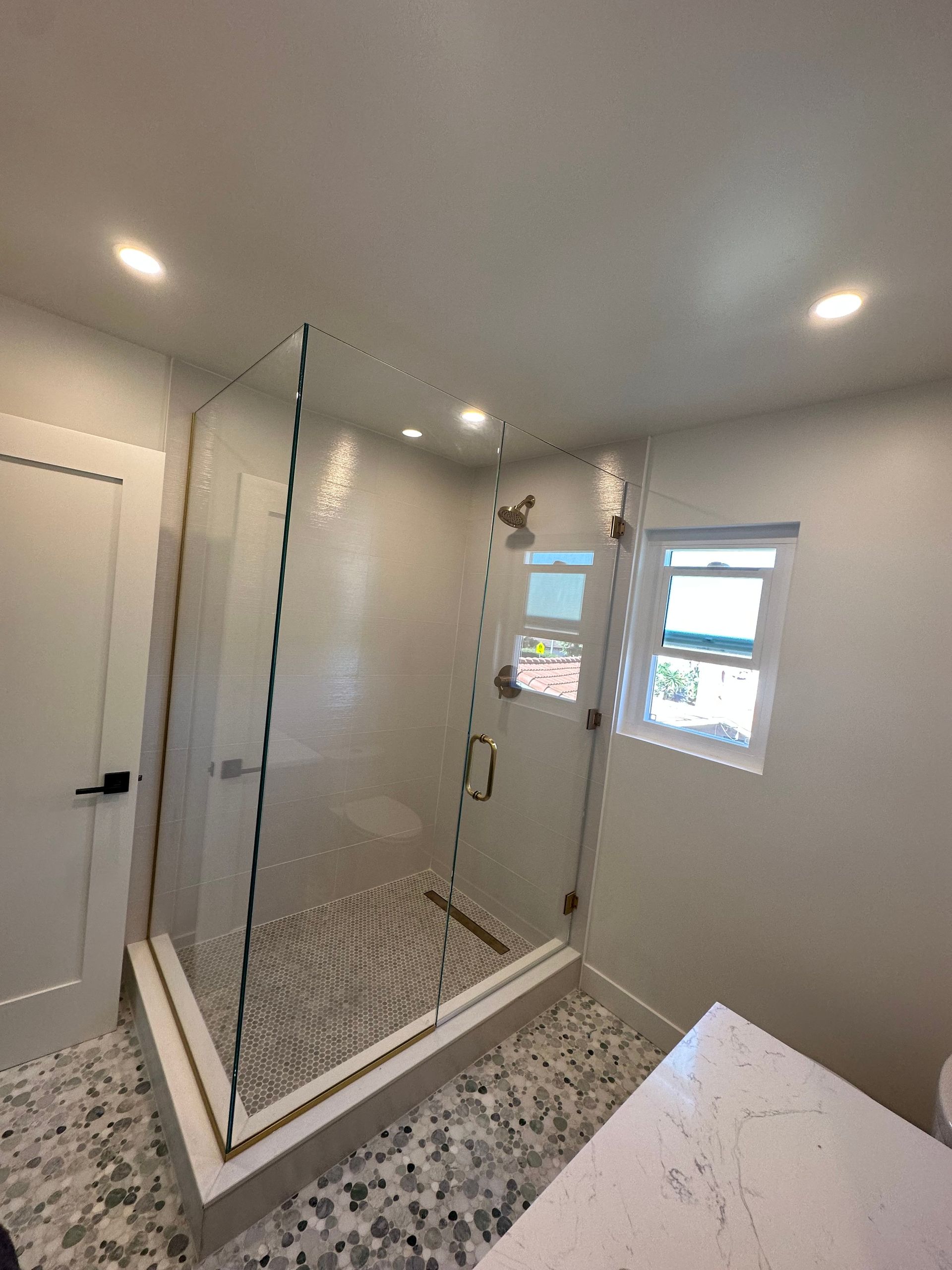 Modern bathroom with glass shower enclosure, mosaic floor, white walls, and a small window.