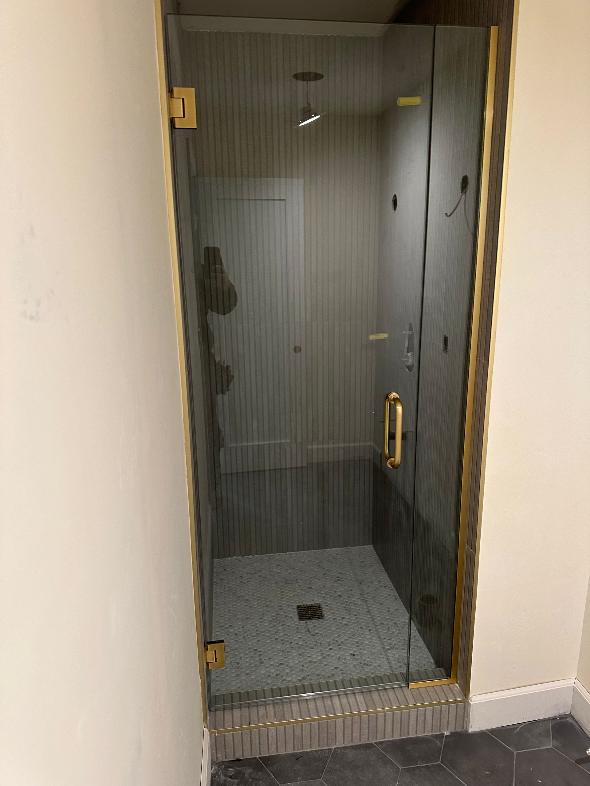Glass shower enclosure with gold hardware, gray tile, and beige walls.