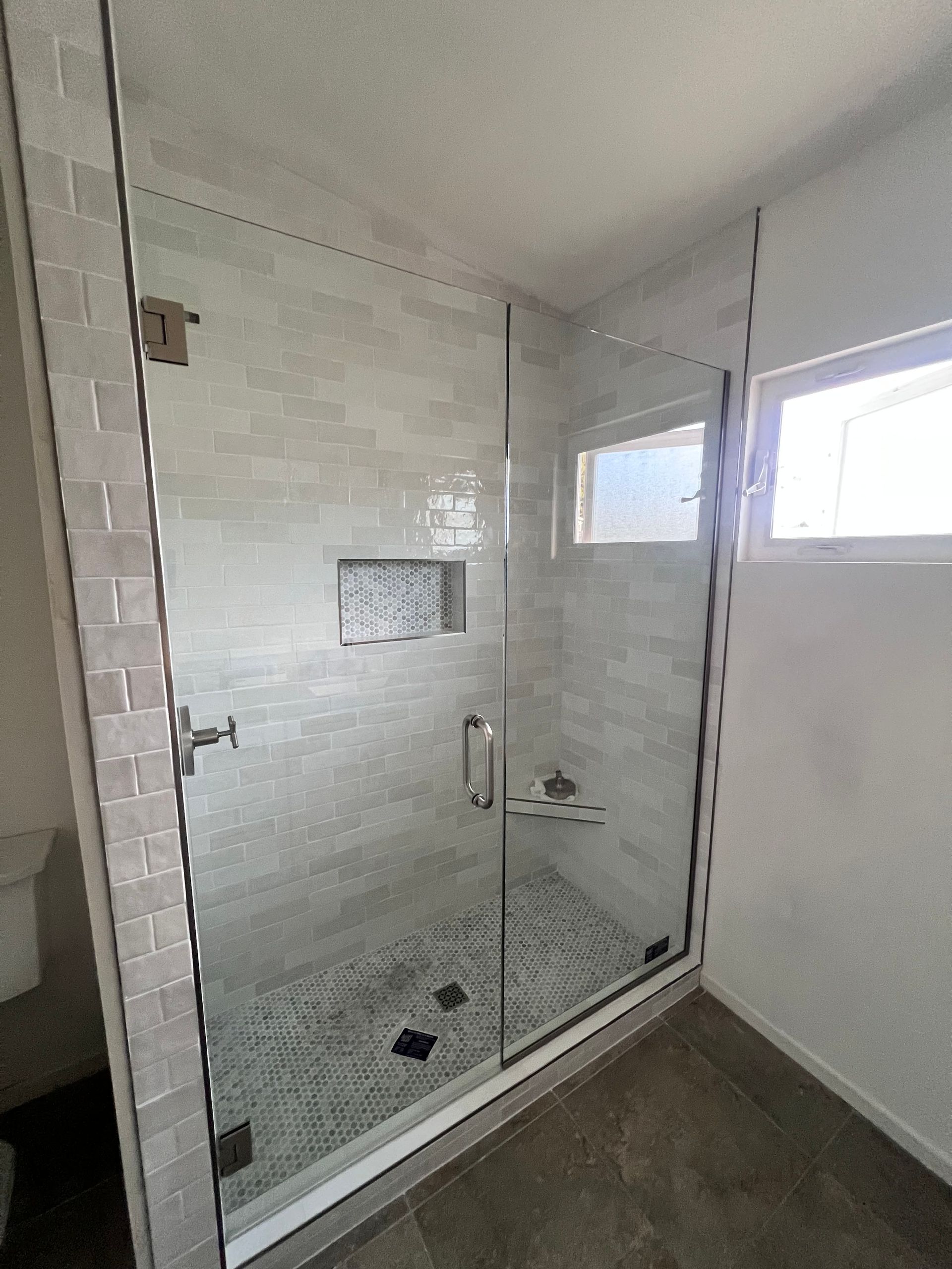 Glass shower enclosure with gray tile walls and mosaic tile niche.