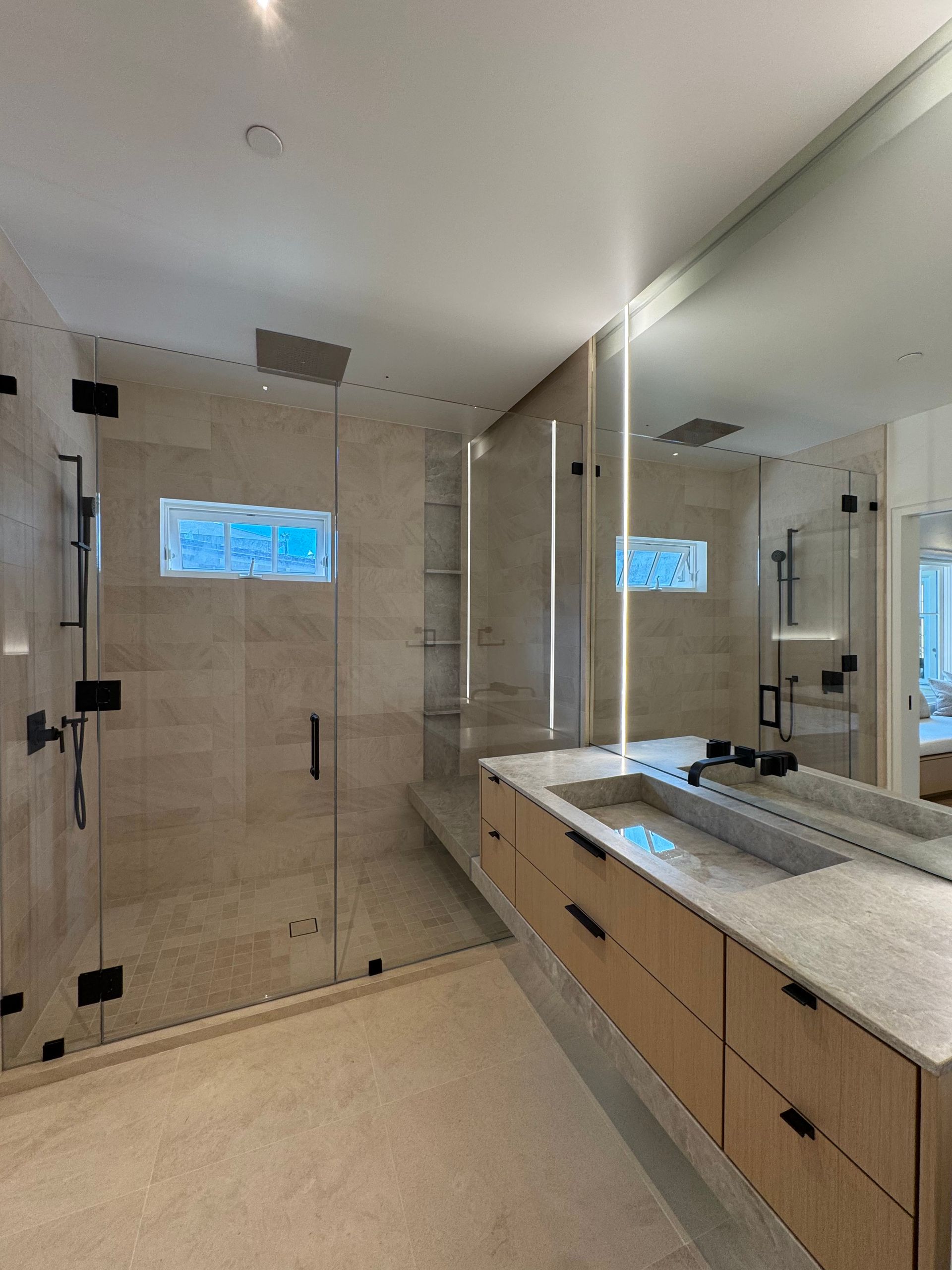 Modern bathroom with glass shower, light wood vanity, and large mirror.