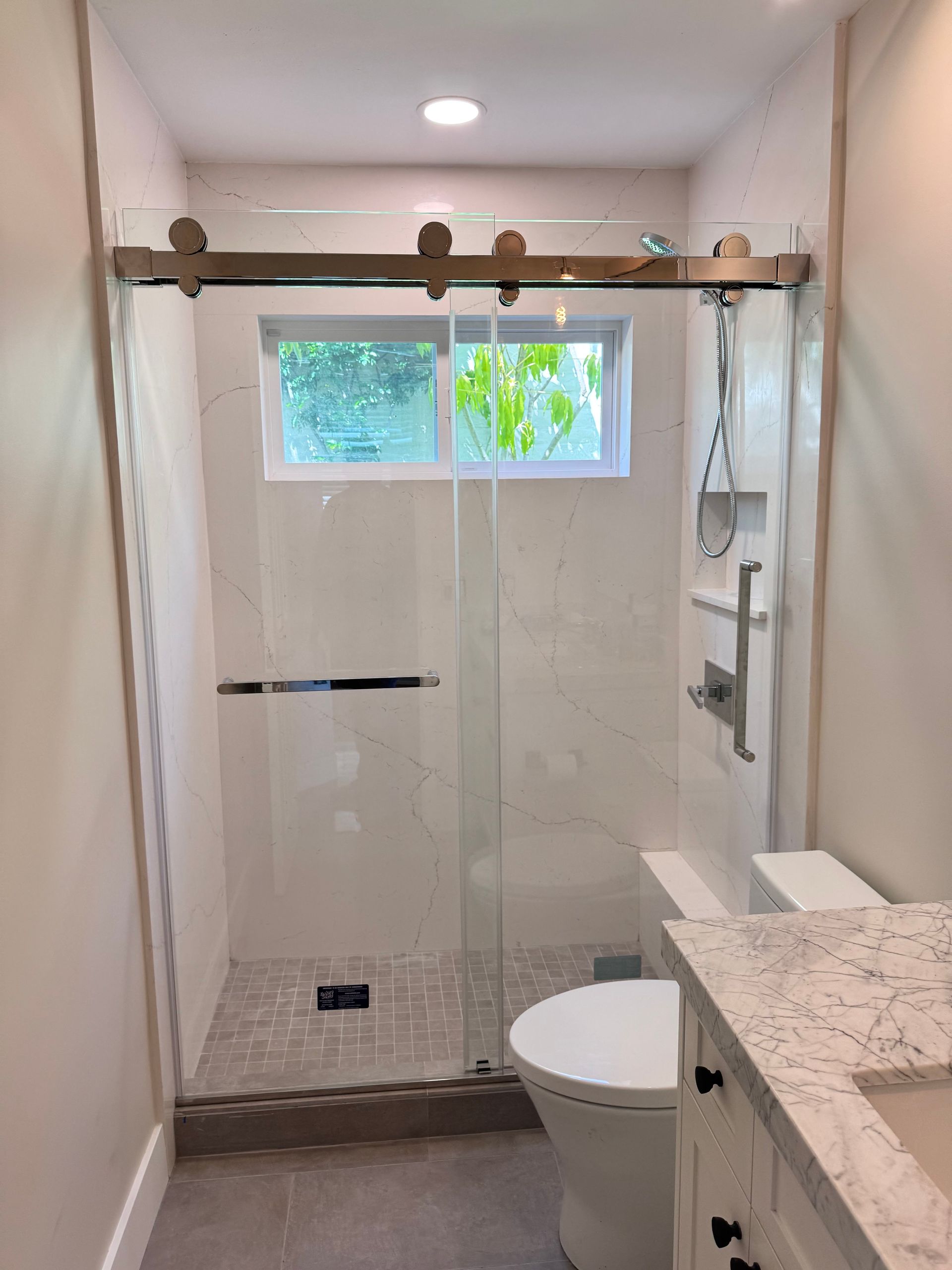 A newly renovated bathroom with a glass shower and sliding door.  The toilet and countertop are visible.