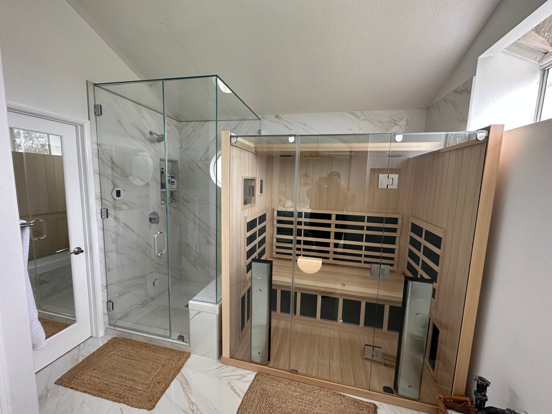 A bathroom with a glass-enclosed shower and a wooden sauna, both with light-colored walls and flooring.