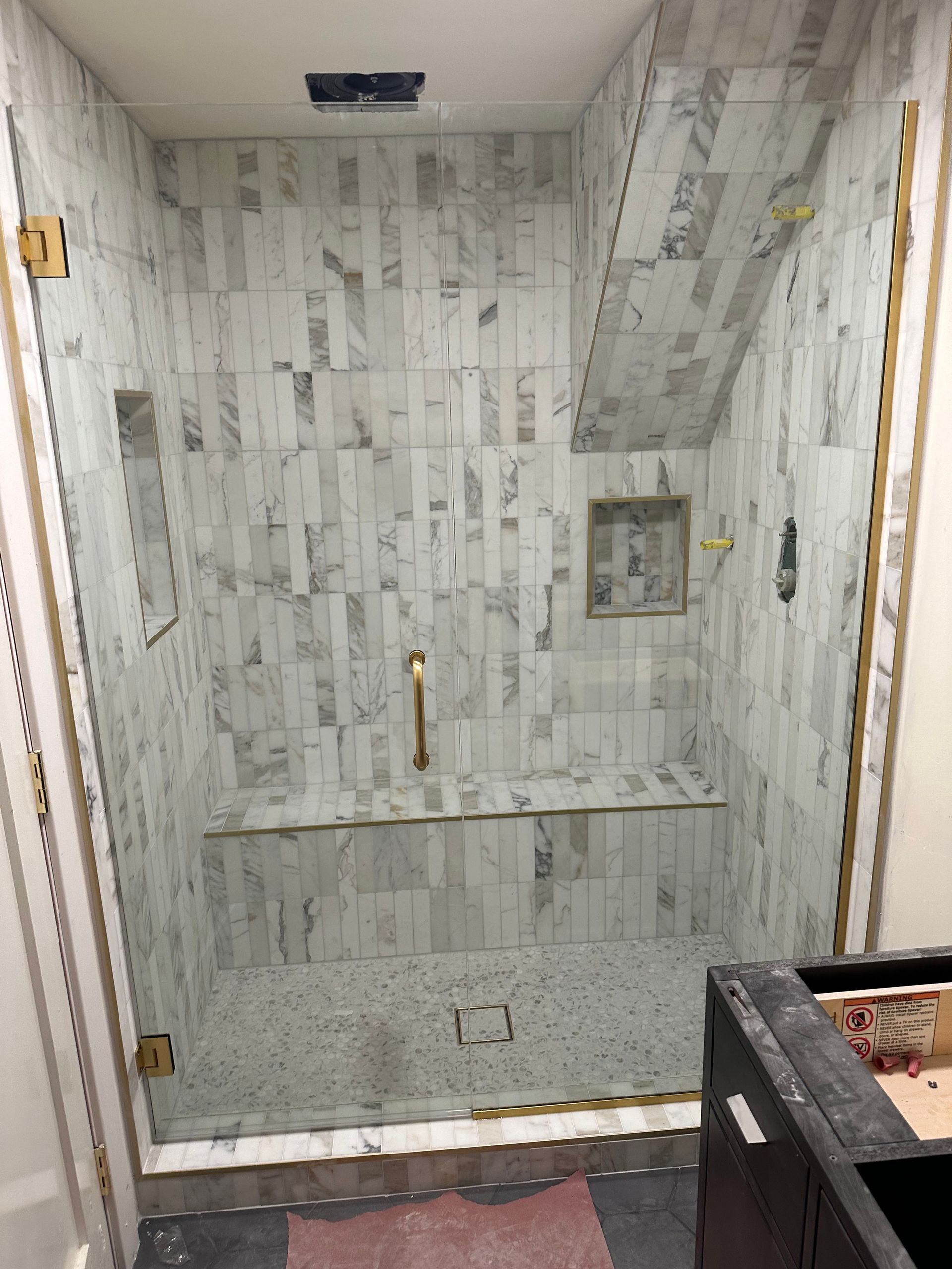 Newly tiled shower with glass door and gold hardware, in a neutral color palette.