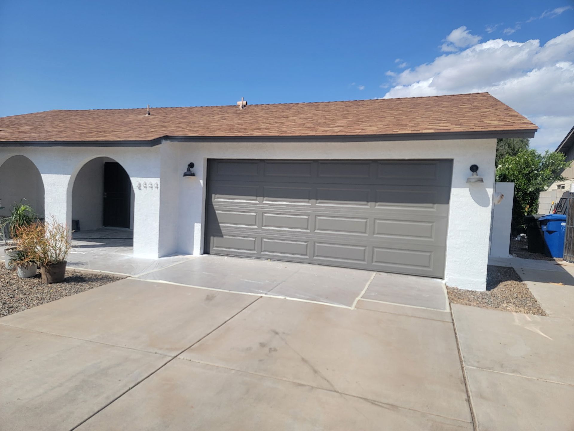 A white house with a gray garage door and a brown roof.