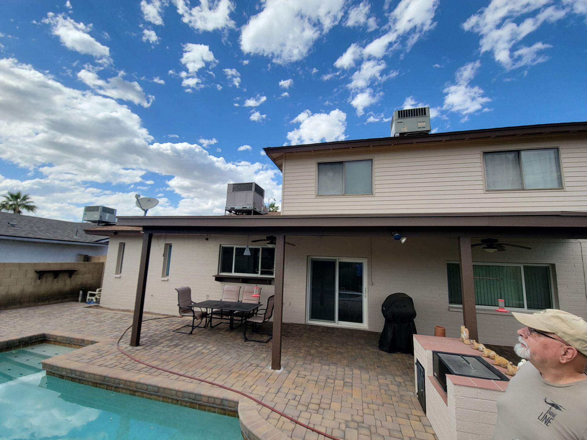 A man is standing in front of a house with a patio and a pool.