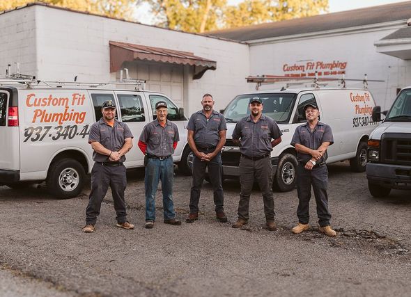Five people in work uniforms standing in front of vans with company logo and phone number.