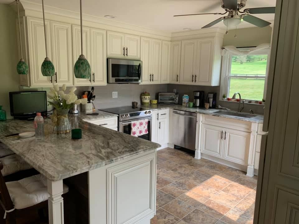 a kitchen with white cabinets , granite counter tops , stainless steel appliances and a ceiling fan .