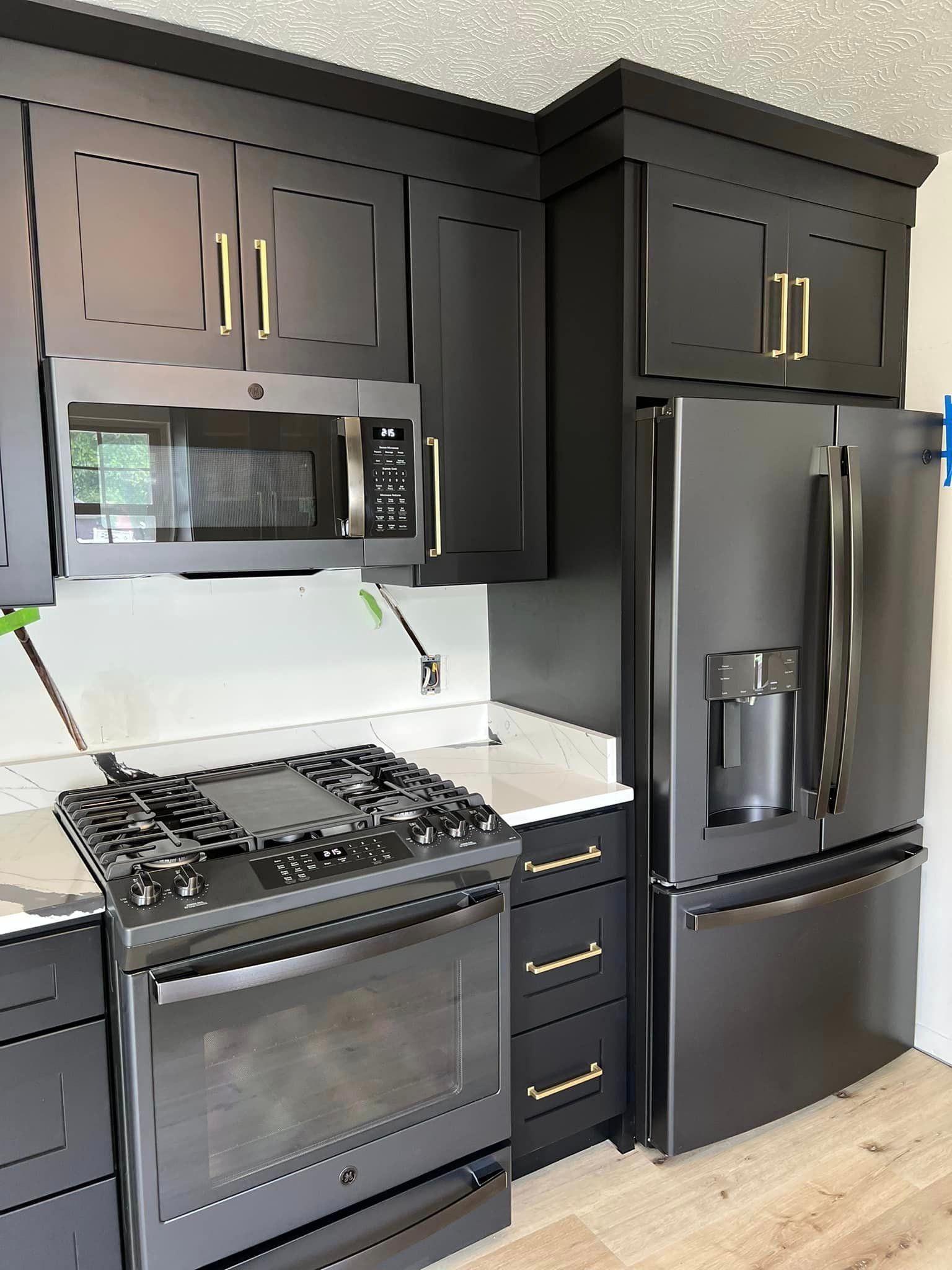 a kitchen with black cabinets , a stove , a refrigerator , and a microwave .