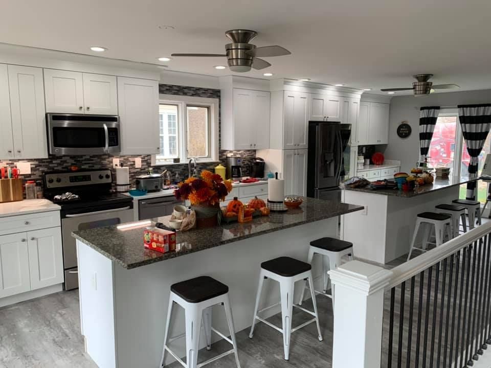 a kitchen with white cabinets , granite counter tops , stools and a ceiling fan .