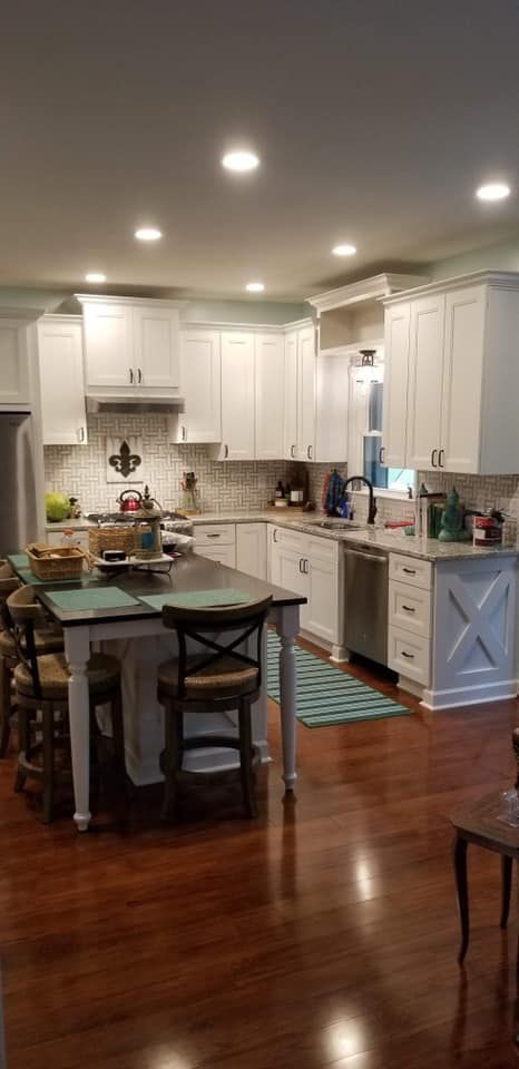a kitchen with white cabinets , hardwood floors , a table and chairs .