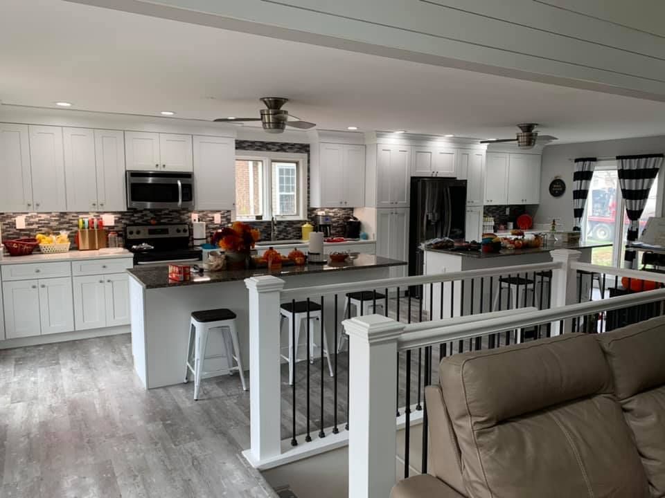 a kitchen with white cabinets , a stove , a refrigerator , a microwave and a couch .