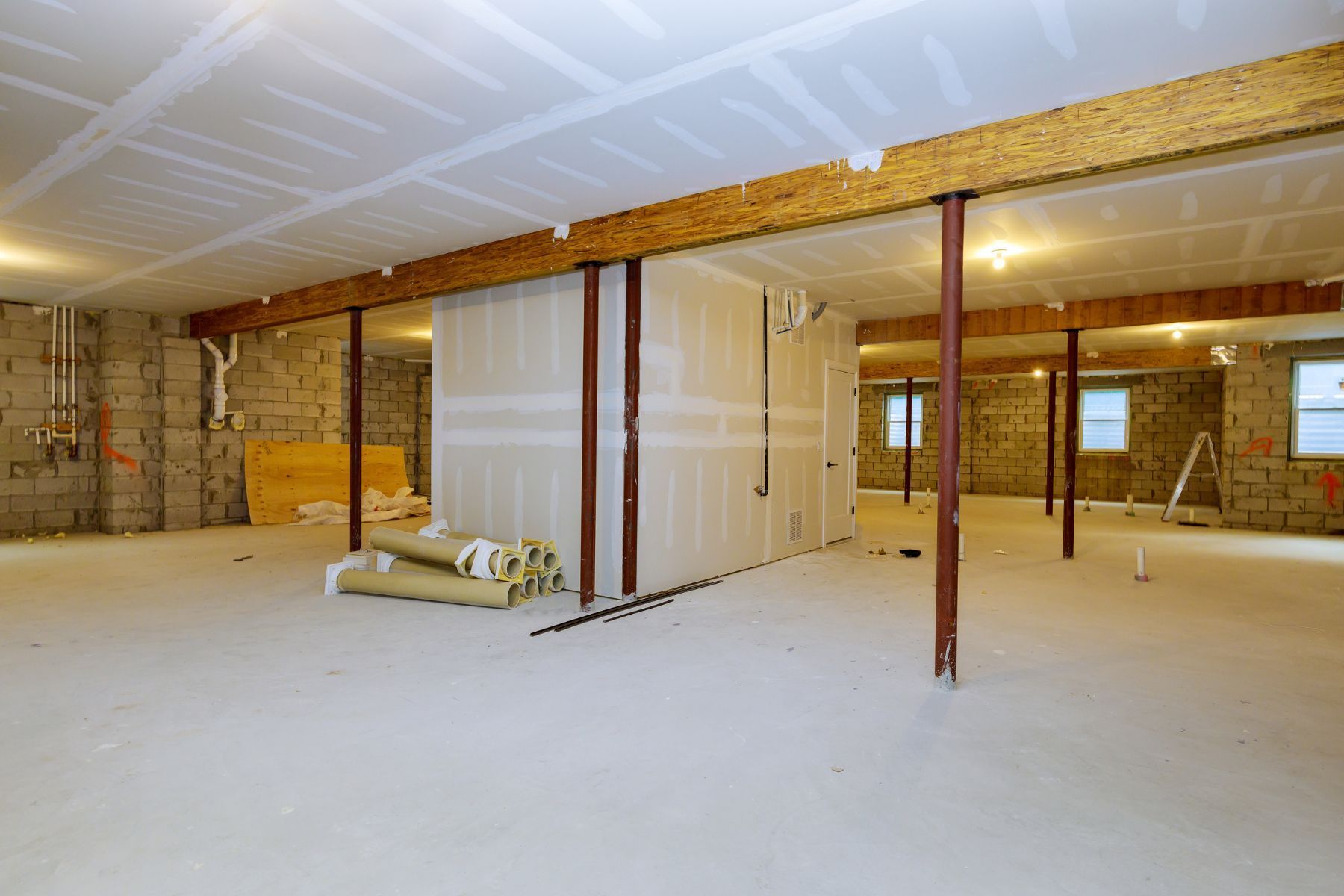 Basement under construction, with exposed beams, support columns, and unfinished walls and ceiling.