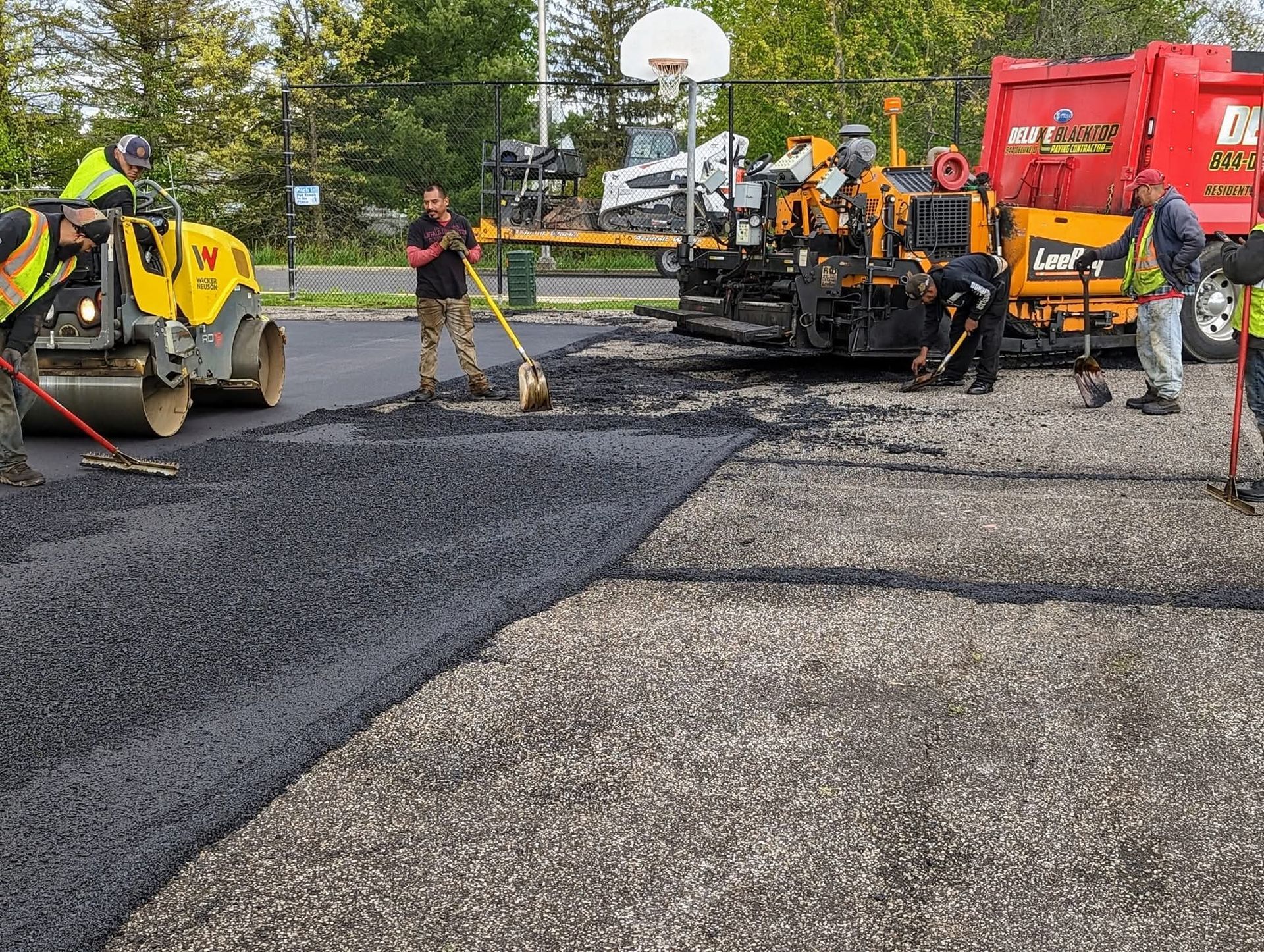 Asphalt paving: Workers laying fresh black asphalt on a gray stone surface with machinery.
