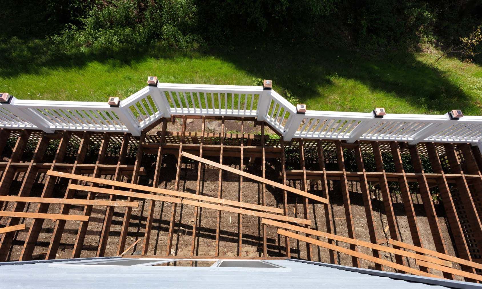 Overhead view of deck under construction, with exposed wooden frame, white railing, and green grass.