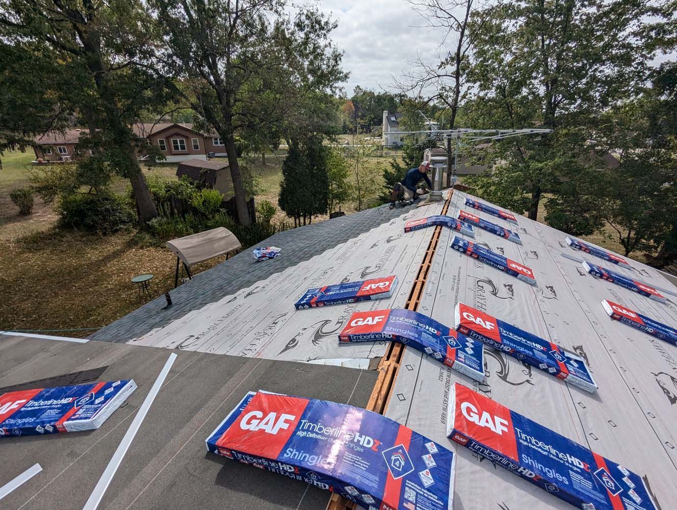 Roof being worked on; new shingles and materials visible, person on roof.