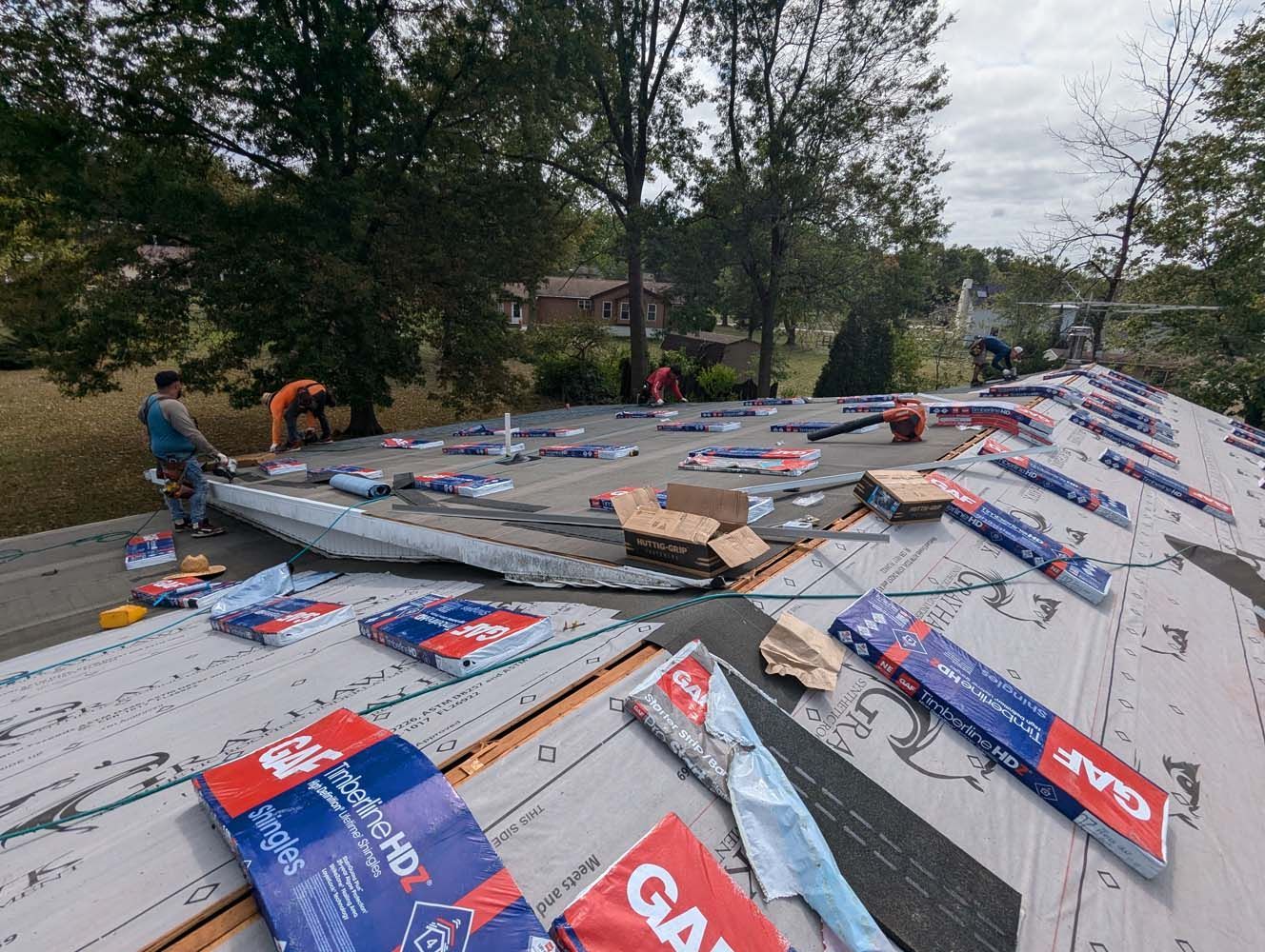 Roofers installing shingles on a house roof on a cloudy day.