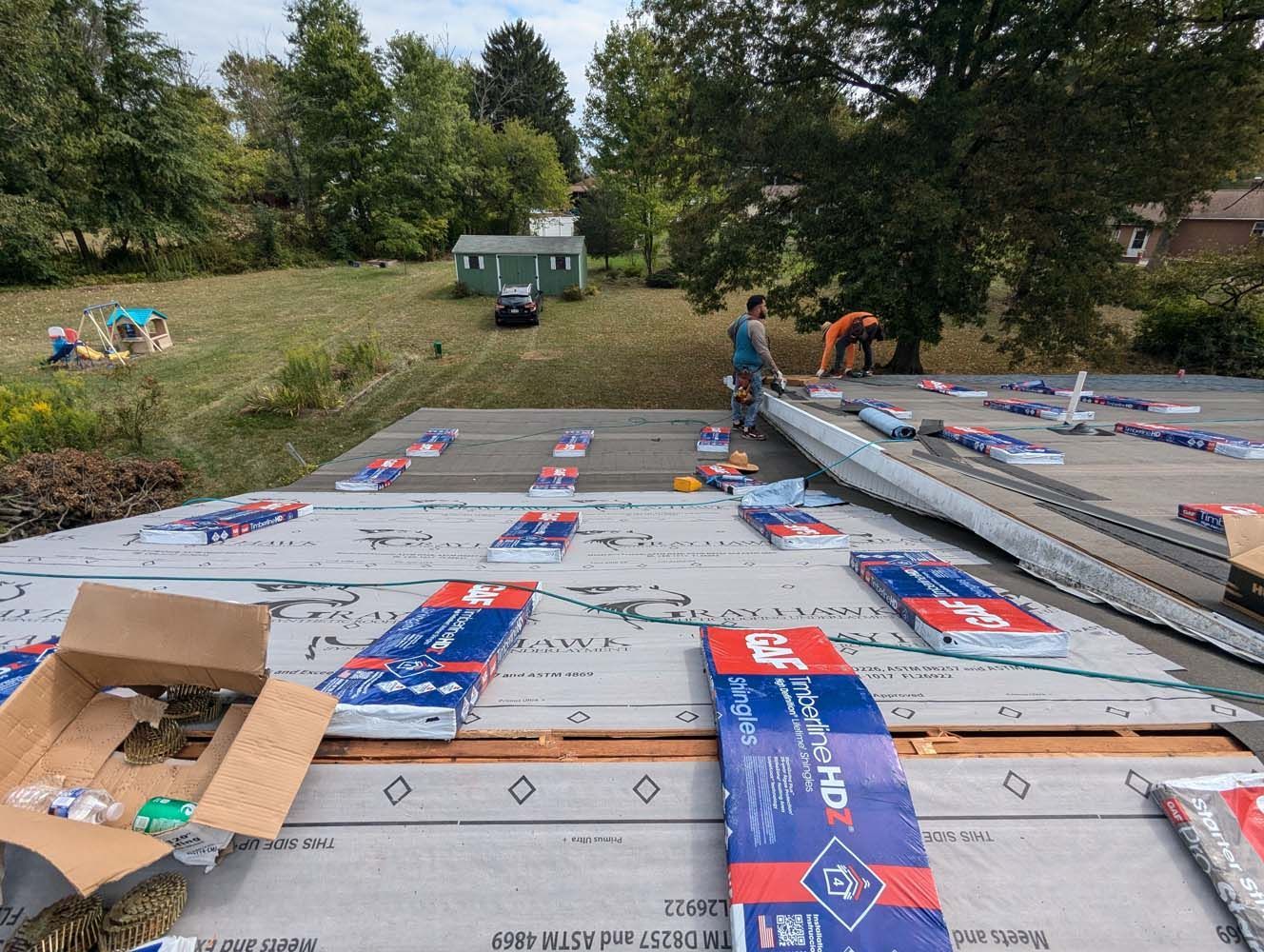 Roofers installing roofing materials on a home with a grassy backyard.