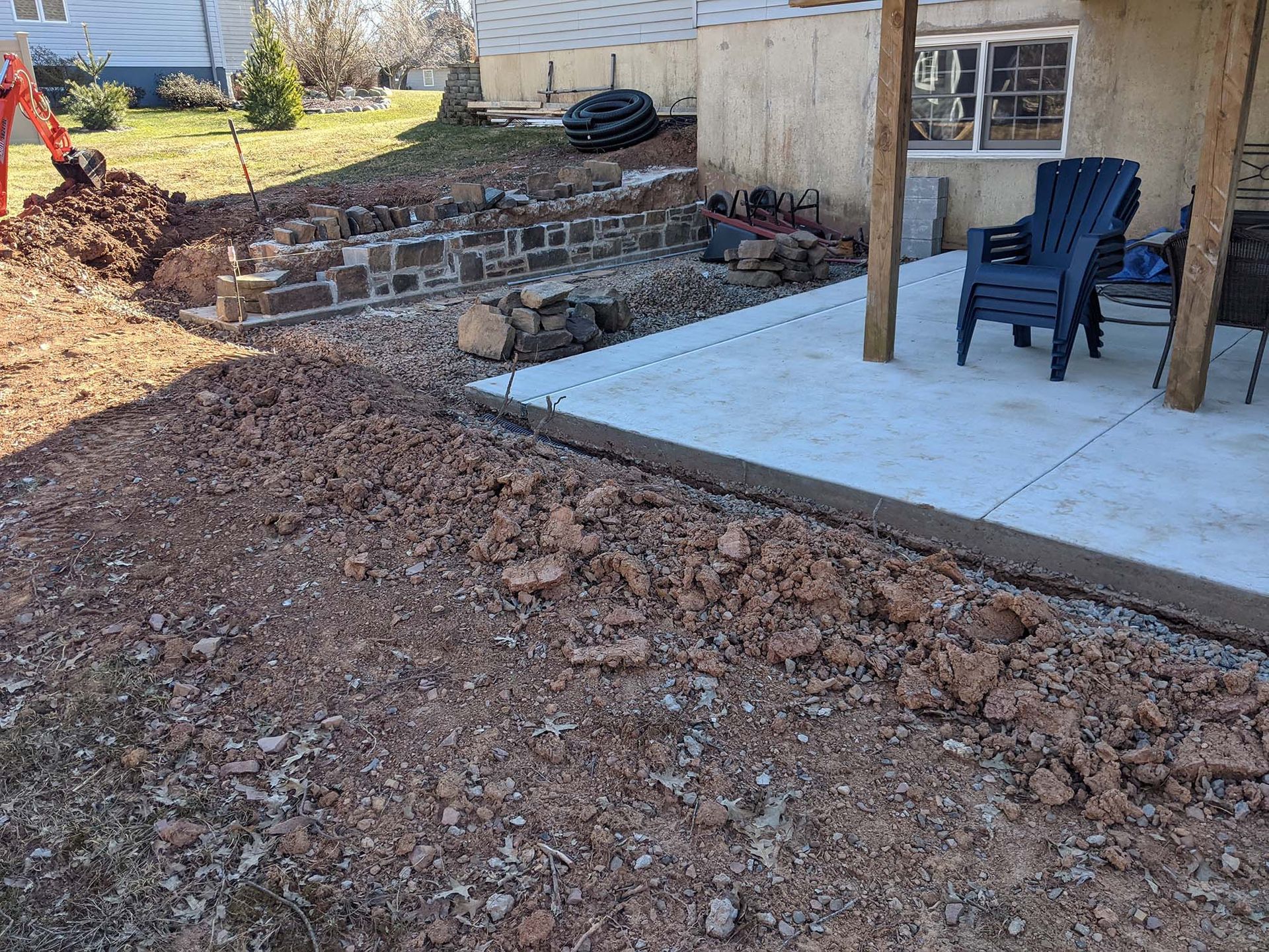 Dirt pile next to a concrete patio, construction site, brick wall, blue chair.