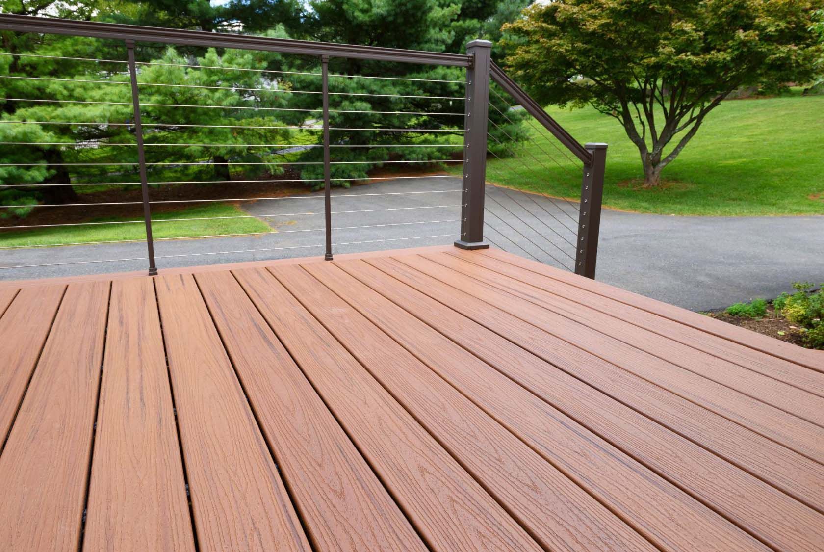 Brown composite deck with cable railing overlooking a green lawn and paved walkway.
