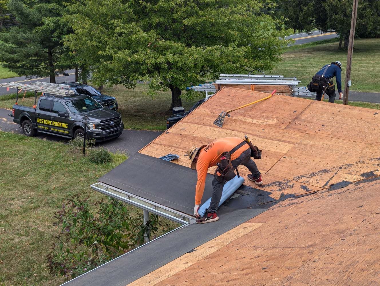Roofers installing roofing material on a house, with a truck nearby.