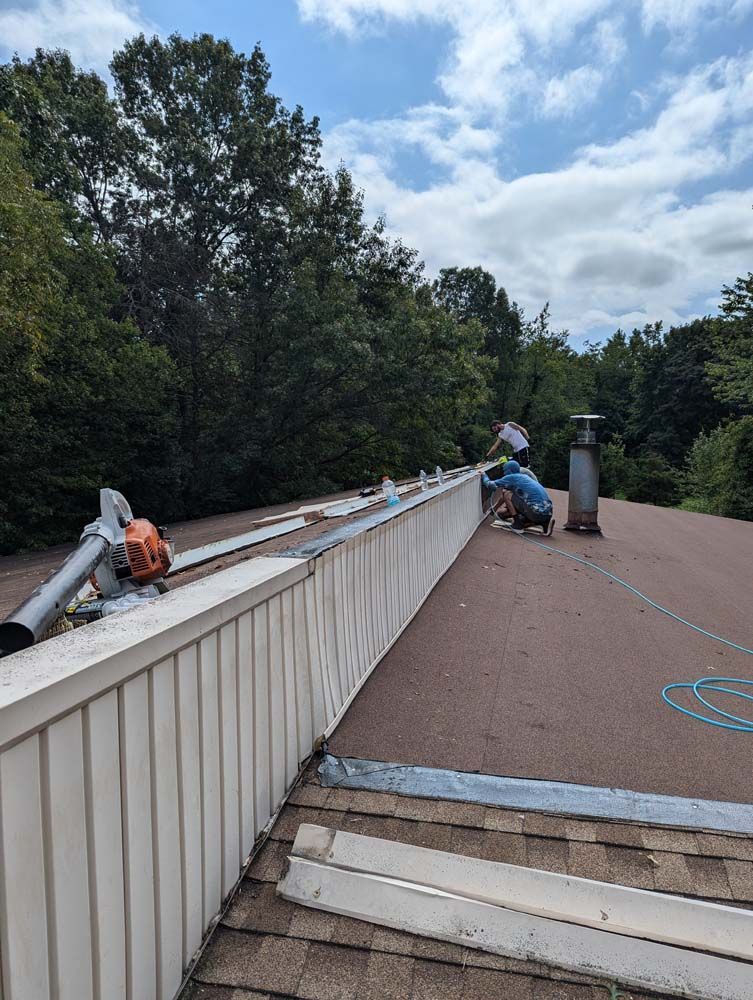 Workers on a roof installing siding on a house, using a leaf blower on a sunny day.
