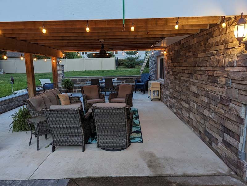 Patio with stone wall, wooden pergola, string lights, and outdoor seating.