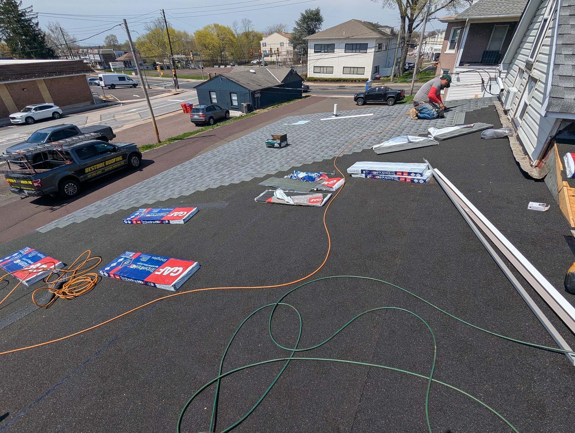 Rooftop with roofing materials and vehicles parked nearby on a sunny day.